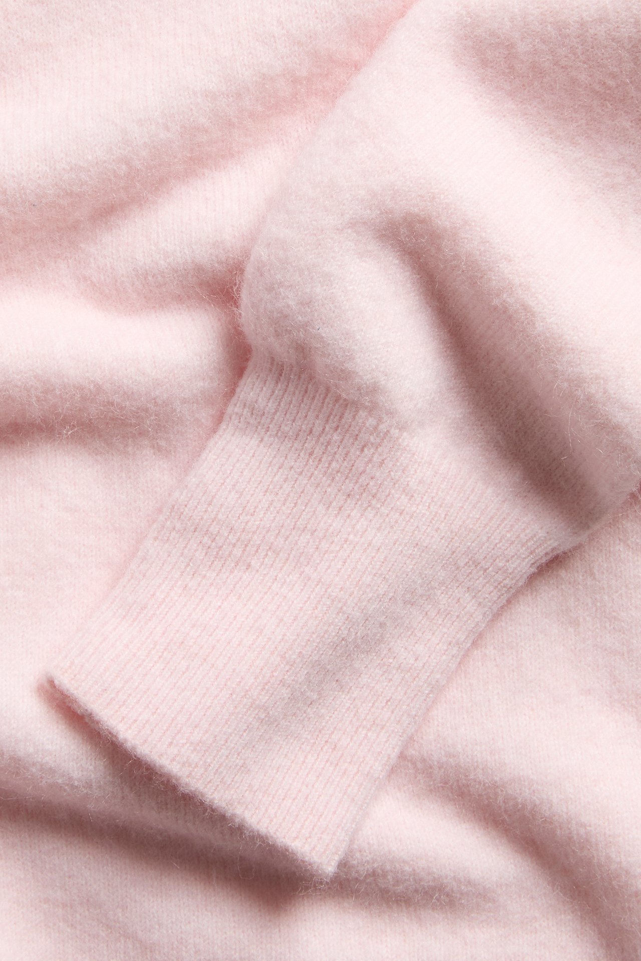 Nærbilde av mykt lys rosa strikket genserstoff med ribbet mansjett, som viser fin tekstur.