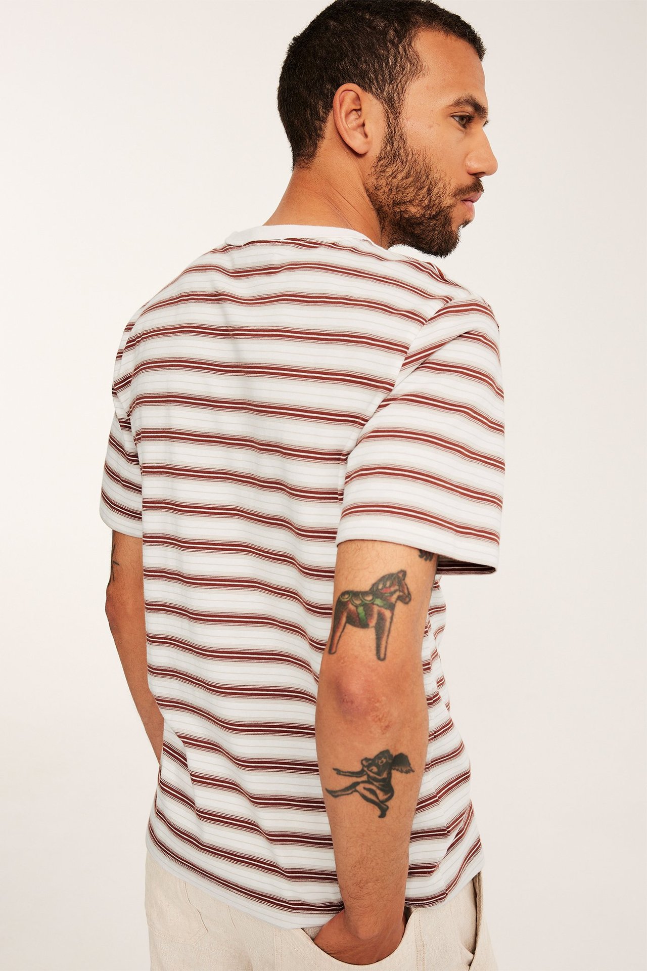 Mies takaa, yllään ruskea- ja luonnonvalkoraidallinen puuvilla t-paita. Normaali istuvuus, vaaleat housut.