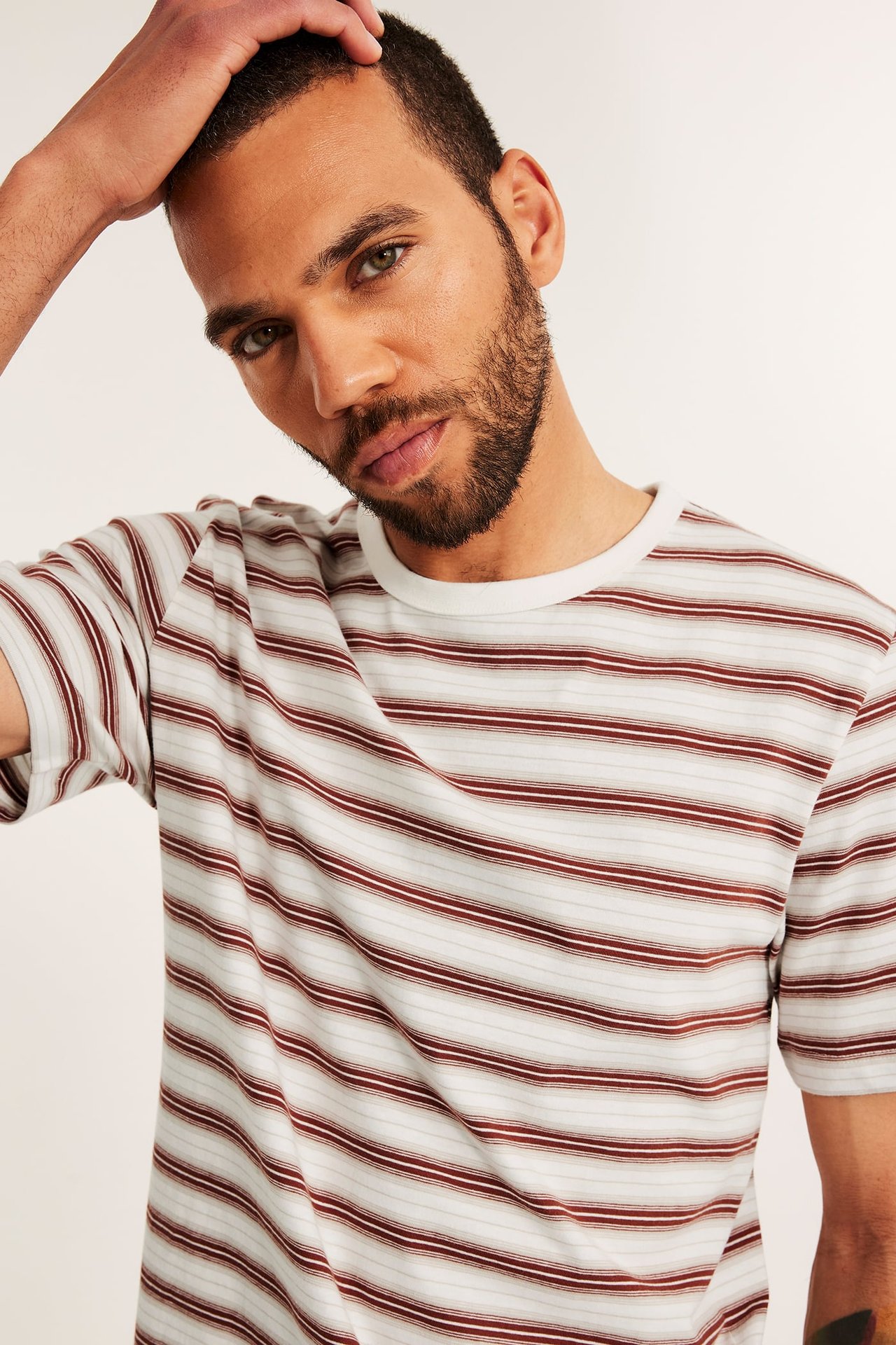Lähikuva edestä: mies yllään regular fit vaaleanharmaa O-aukko puuvillainen t-paita ruskeilla raidoilla.