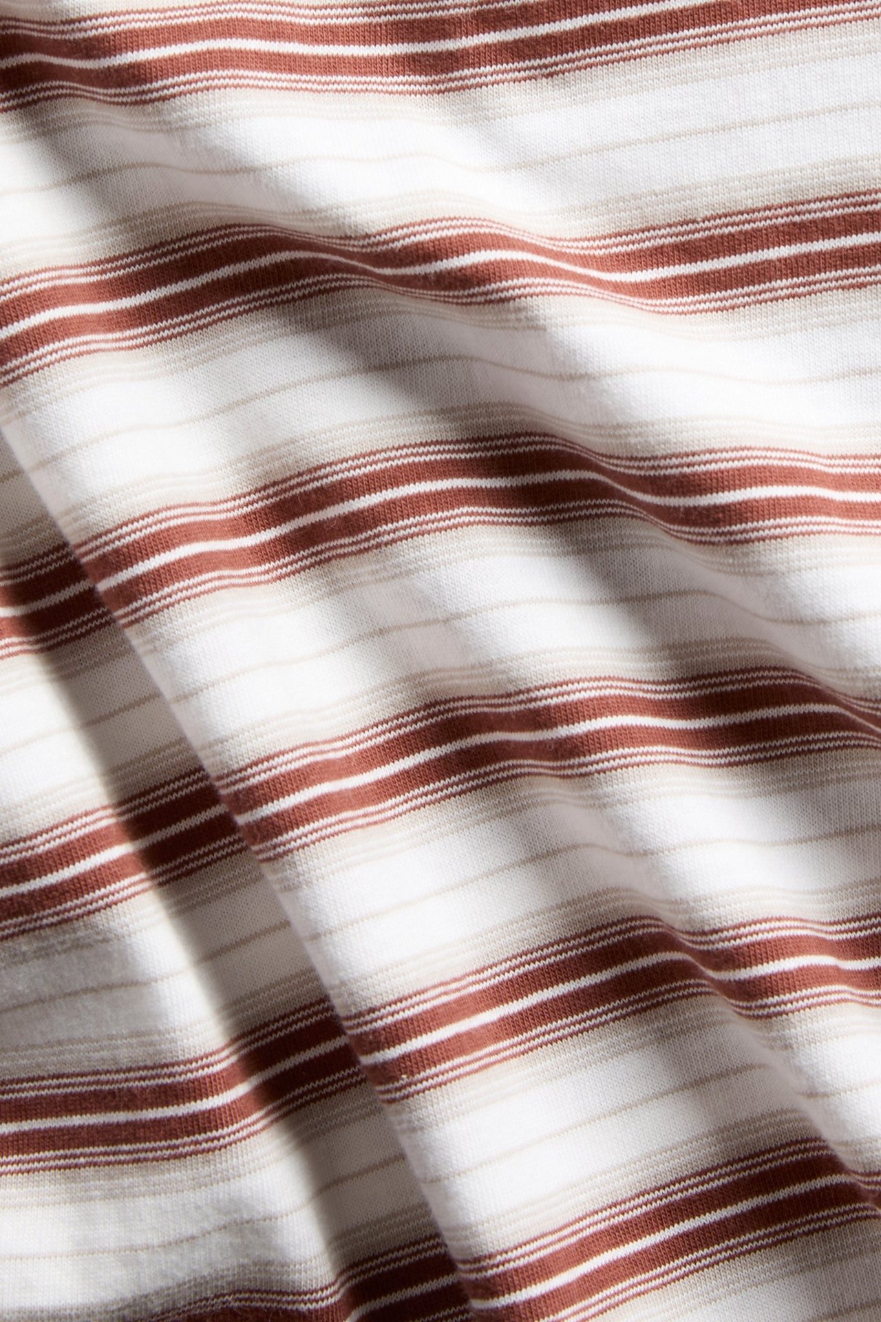 Lähikuva ruskeasta ja valkoisesta raidallisesta puuvilla-T-paidan kankaasta.