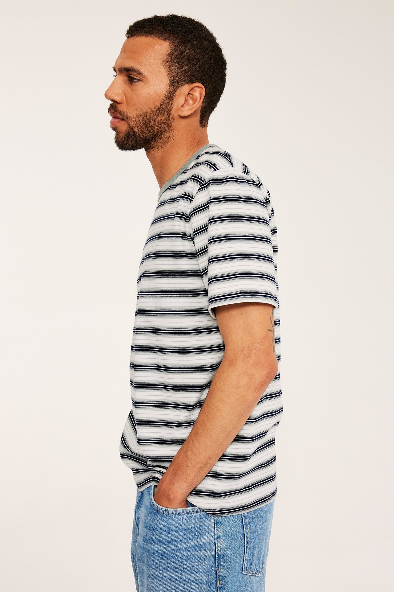 Sivukuva: Mies tummansininen, vaaleansininen, valkoraidallinen puuvilla T-paita ja vaaleansiniset farkut.