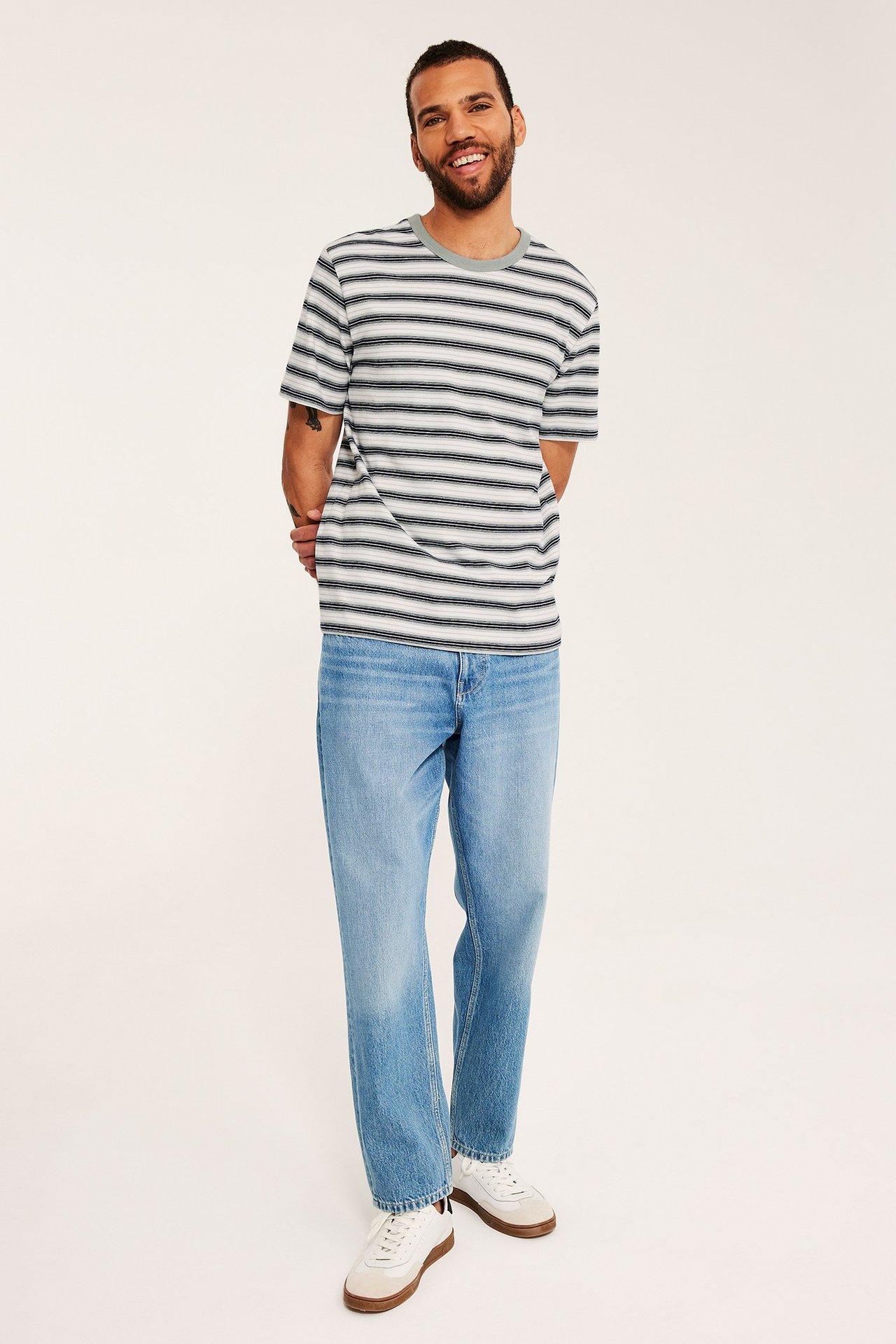 Edestäpäin: mies tummansiniraitaisessa puuvillaisessa t-paidassa, vaaleansinisissä farkuissa, valkoisissa tennareissa.