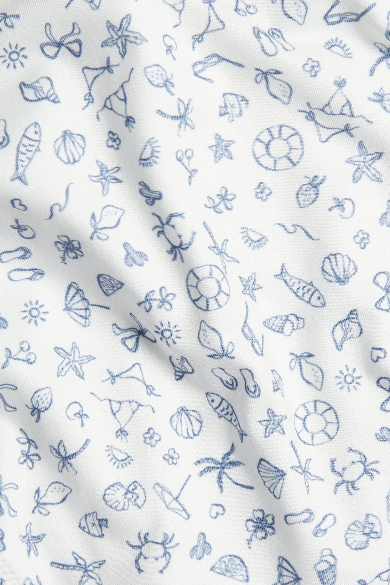 Zbliżenie beżowo-białej, wzorzystej tkaniny fig bikini z niebieskimi letnimi motywami.