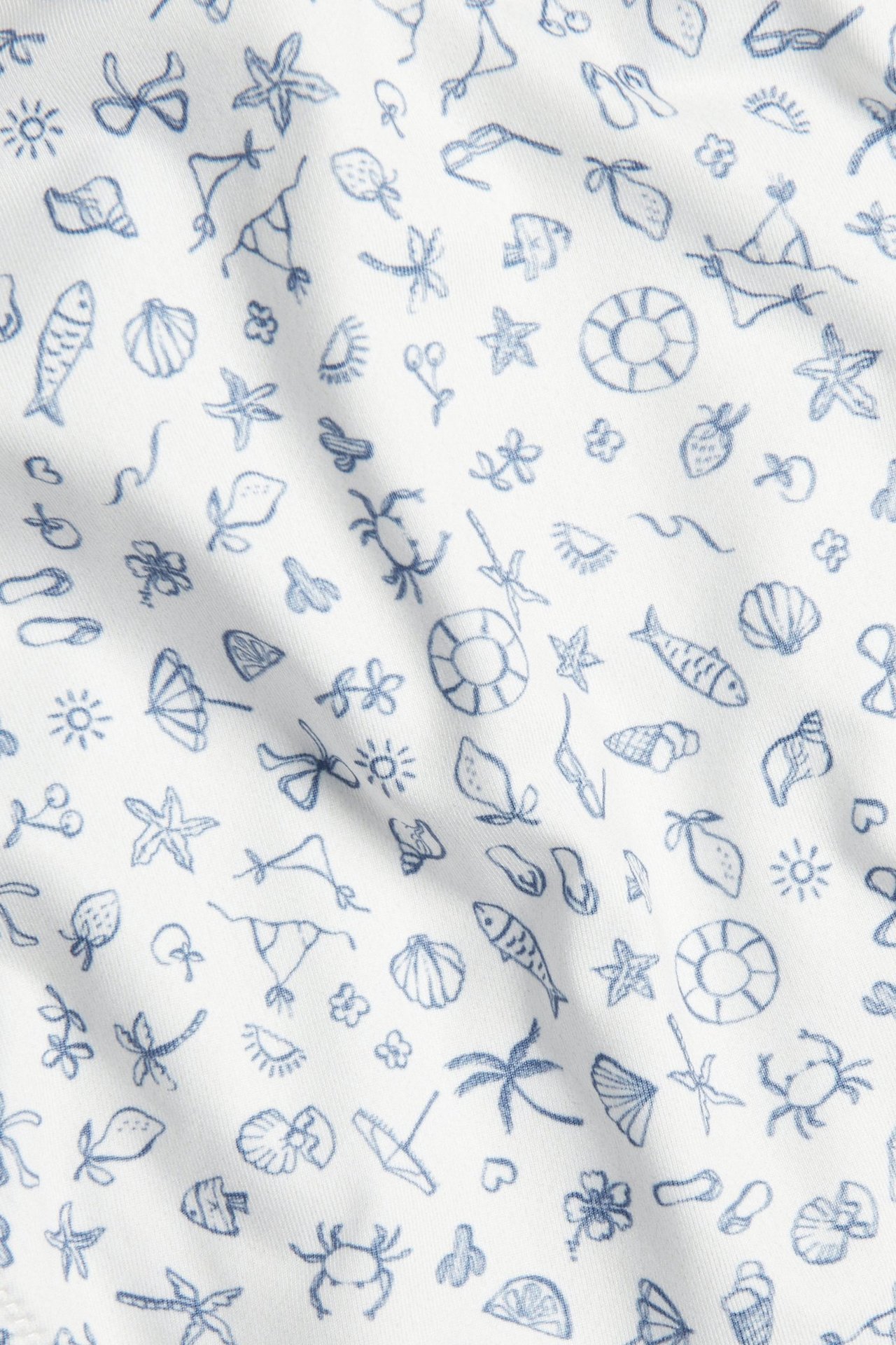 Zbliżenie beżowo-białej, wzorzystej tkaniny fig bikini z niebieskimi letnimi motywami.