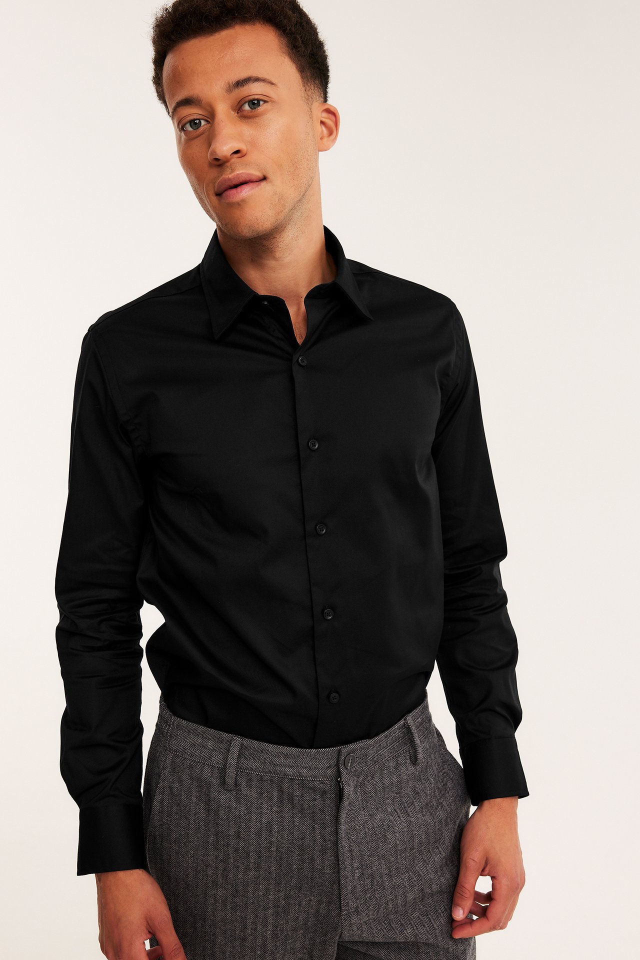 Framsida av manlig modell i svart långärmad skjorta med knappar och grå byxor.