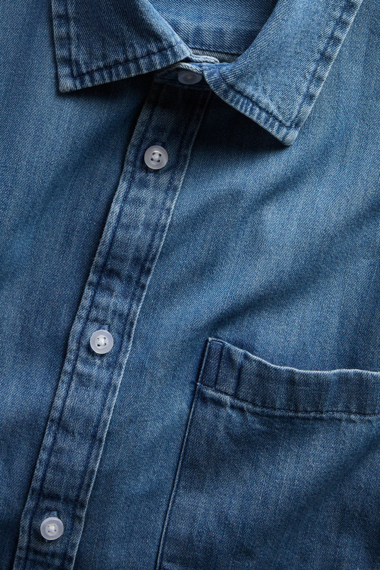 Närbild på en blå denimskjorta med krage, knappslå och bröstficka.
