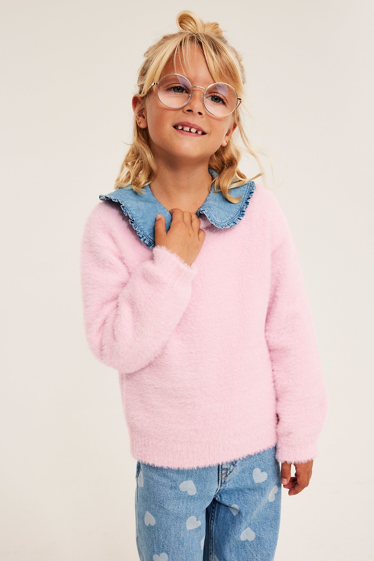 Framifrån: barn i rosa lurvig tröja med jeanskrage och ljusblå jeans med hjärtmönster.