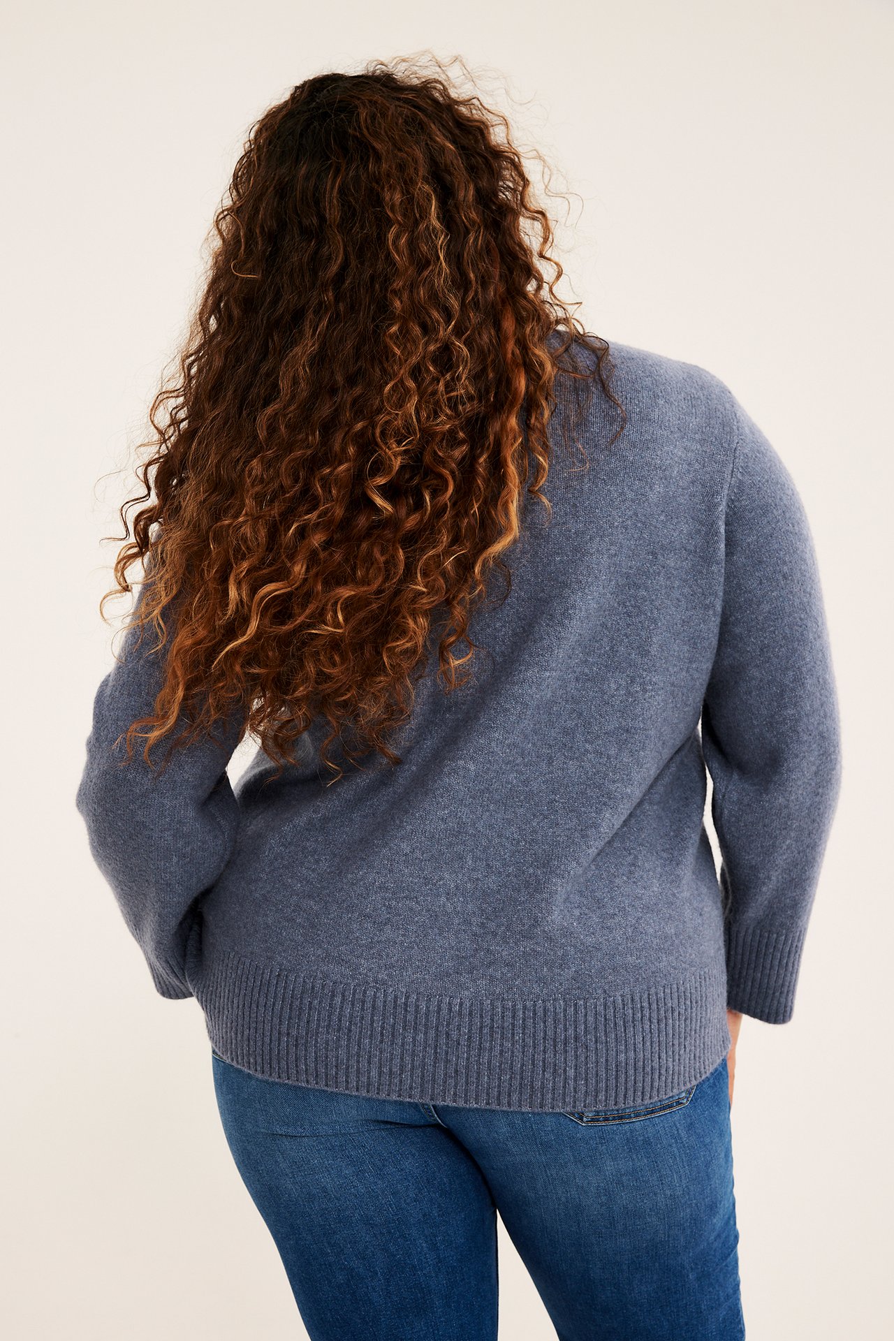 Ryggvisning av en kvinne iført en blå langermet genser og blå jeans.