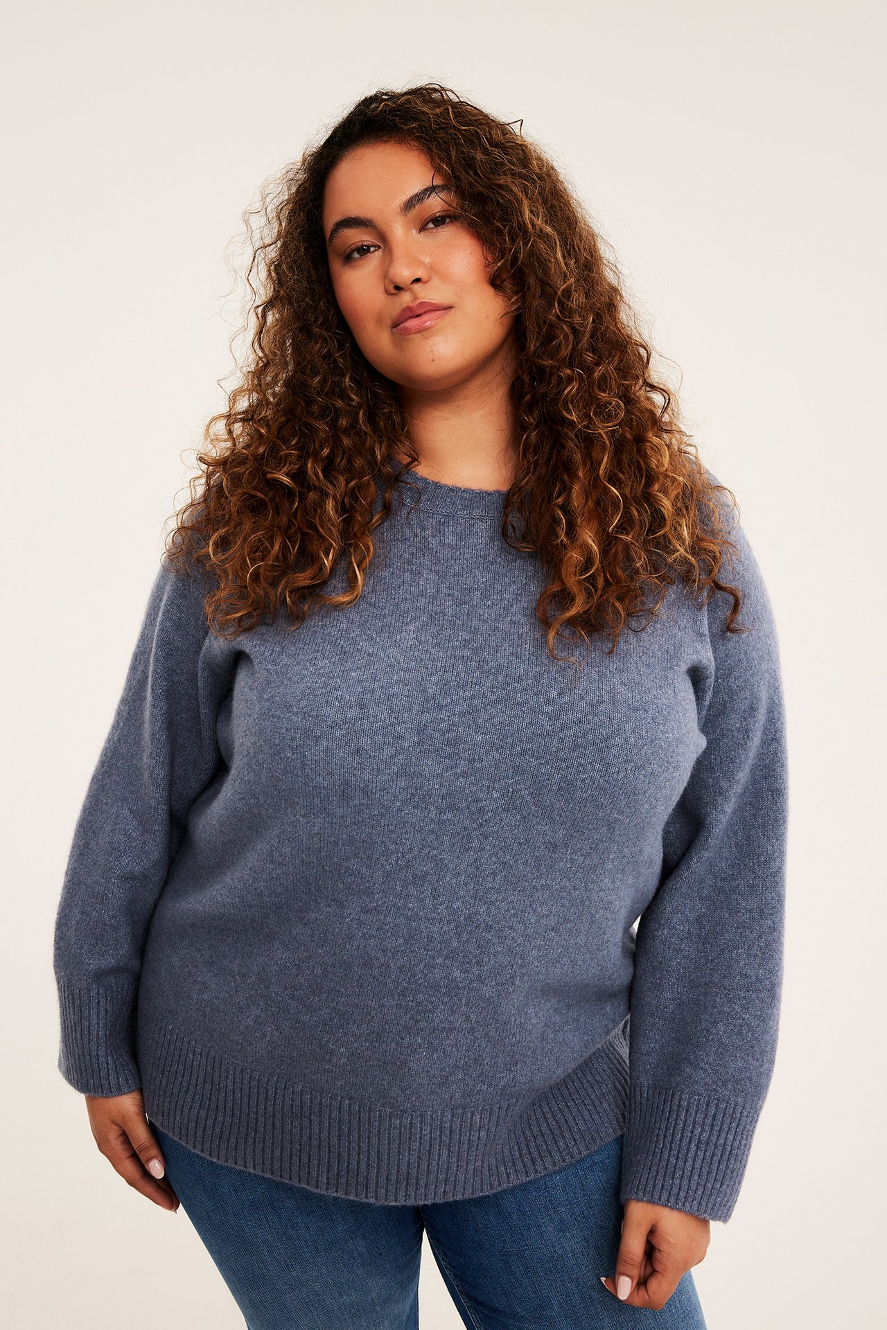 Framsida av en kvinna som bär en blå långärmad stickad tröja och blå jeans.