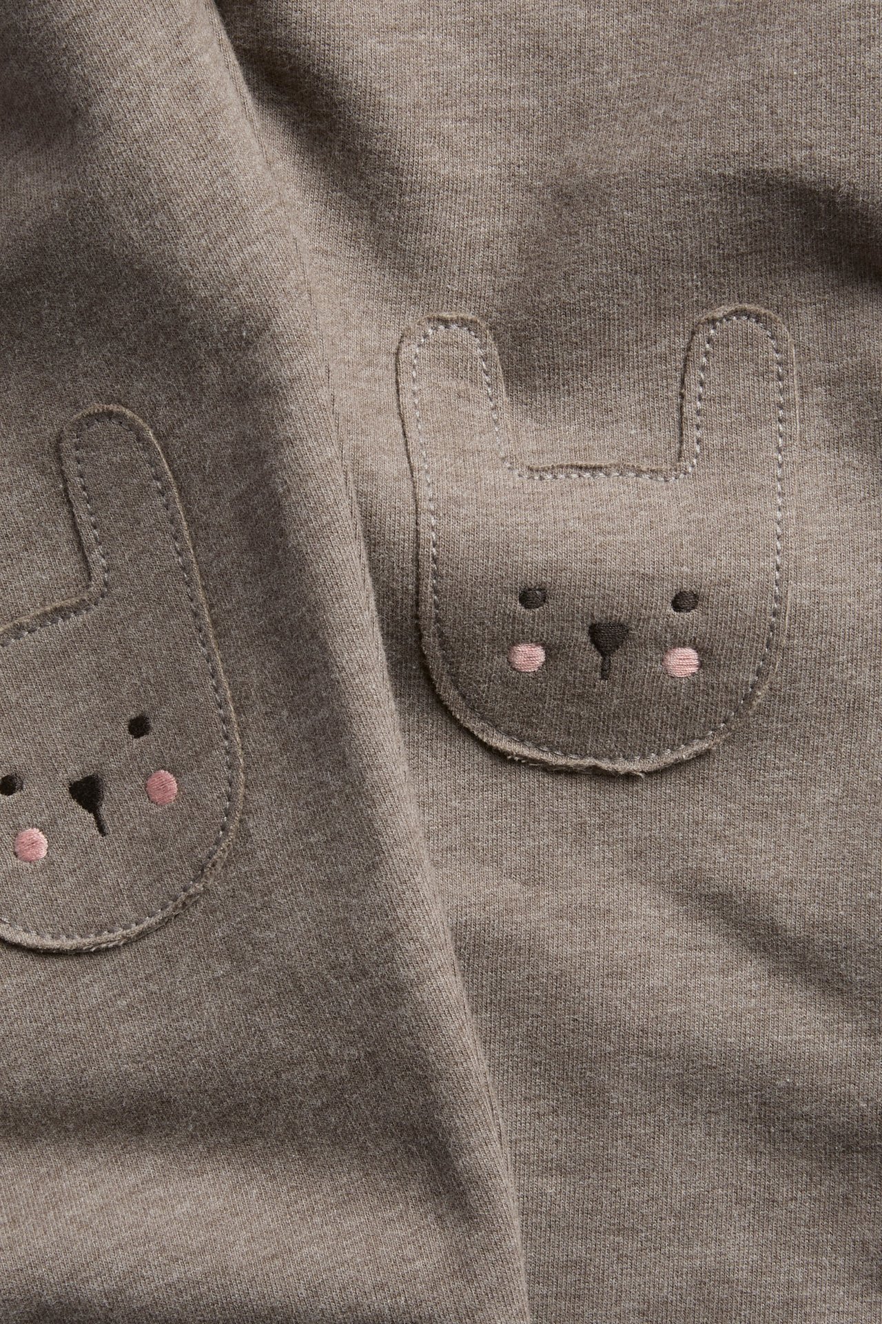 Nærbilde av brunt jerseystoff med to kaninansiktslommer, svarte øyne og rosa kinn.
