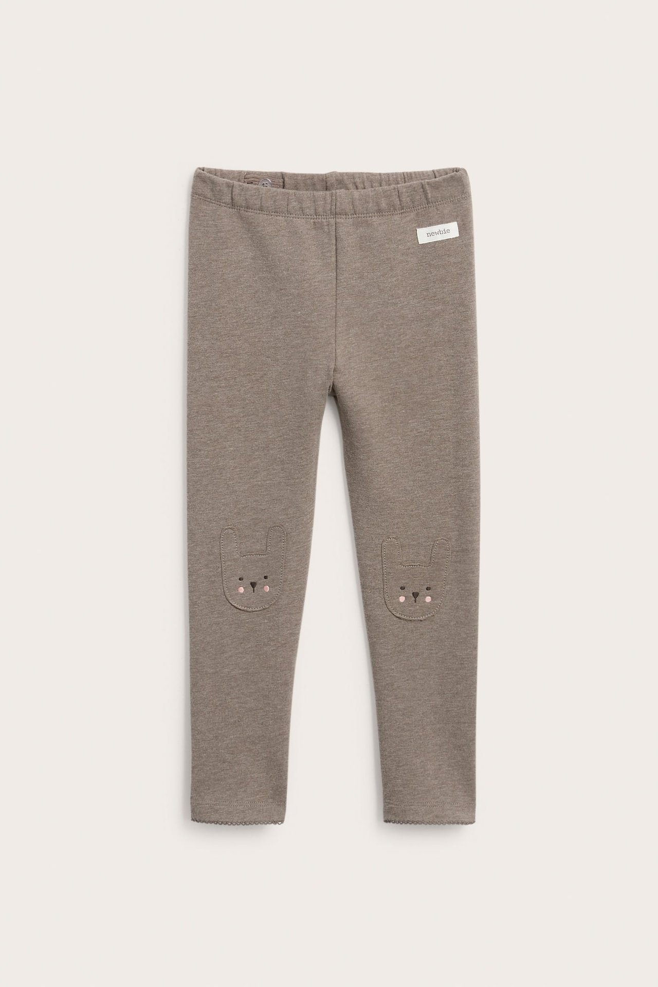 Forfra, taupe baby leggings med kaninøre-lapper på knærne og en 'newbie' etikett.