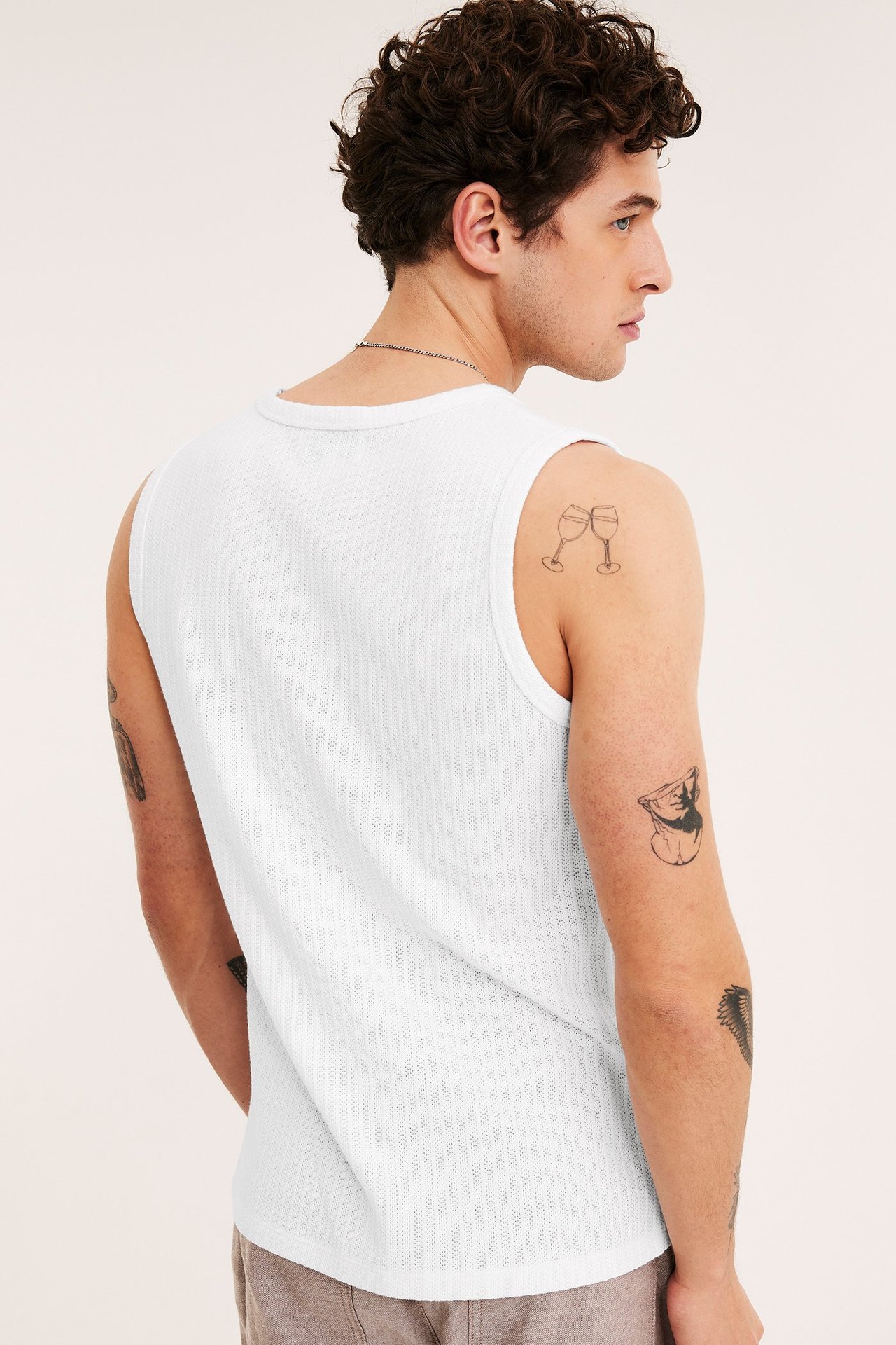 Ryggvy av en man i vitt pointelle slim fit linne, silverkedja och bruna shorts.