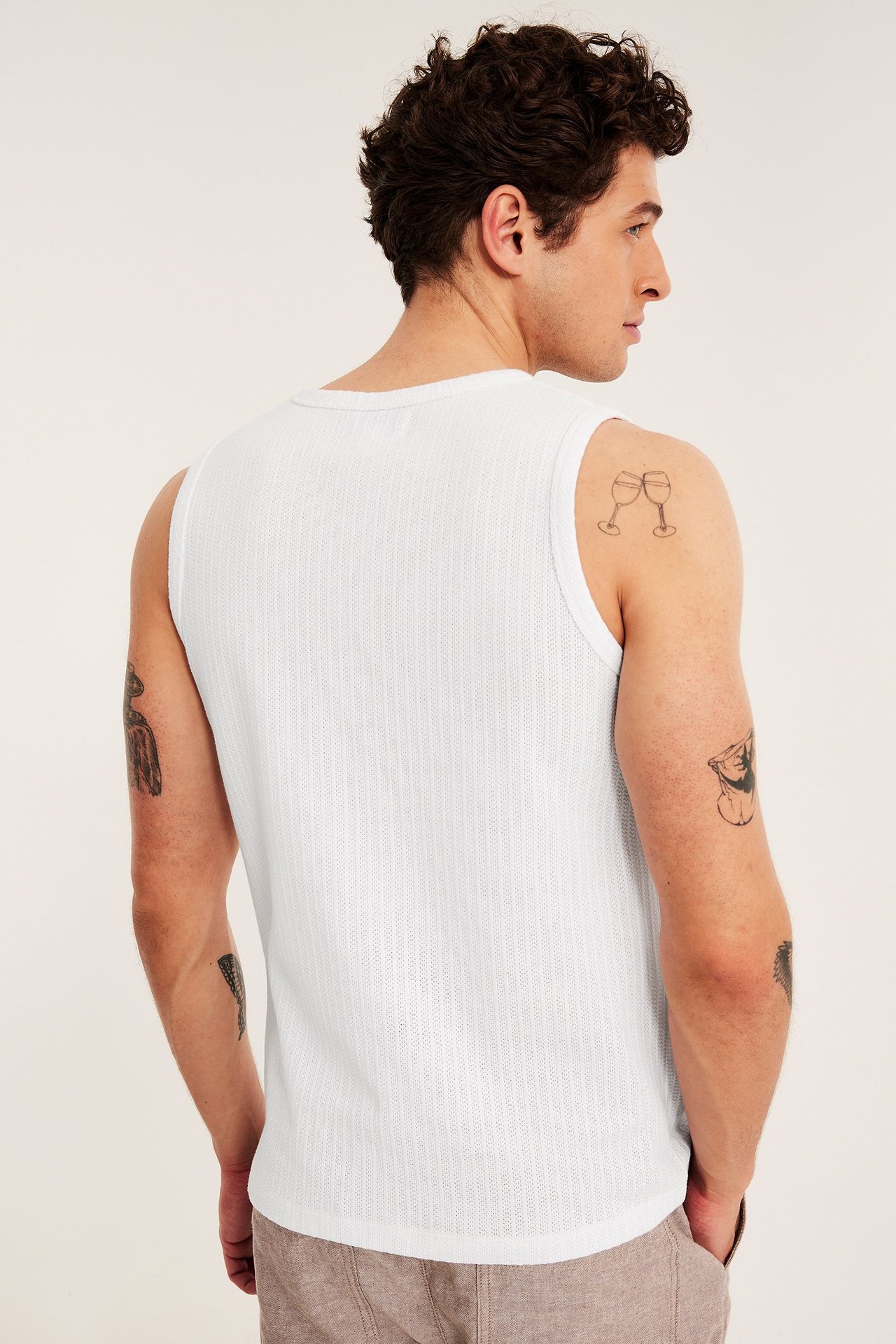 Bakifrån på man i vitt pointelle slim-fit linne och ljusbruna byxor.