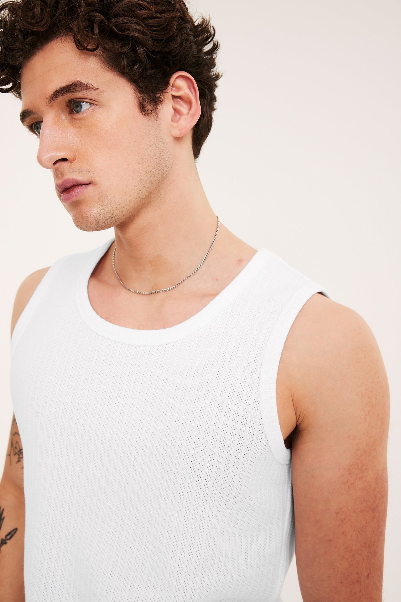 Närbild framifrån av en man i vitt slim fit pointelle linne och en tunn silverkedja.