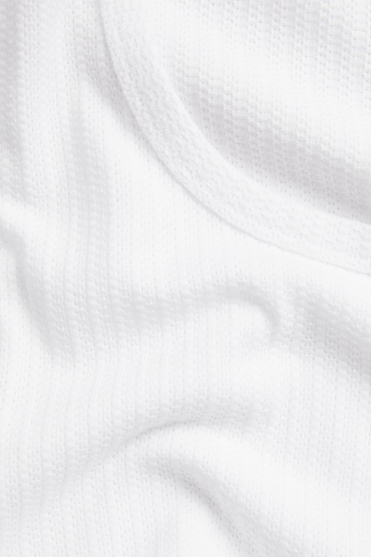 Närbild av vitt pointelle jacquardstickat linne med synlig ribbad kant.