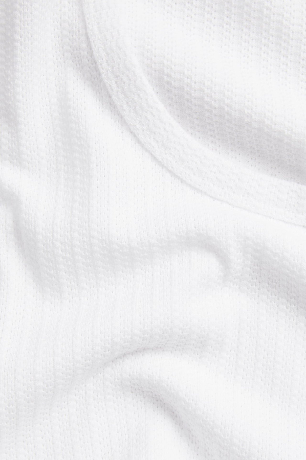 Nærbilde av hvit pointelle jacquardstrikket singletstoff med synlig ribbekant.