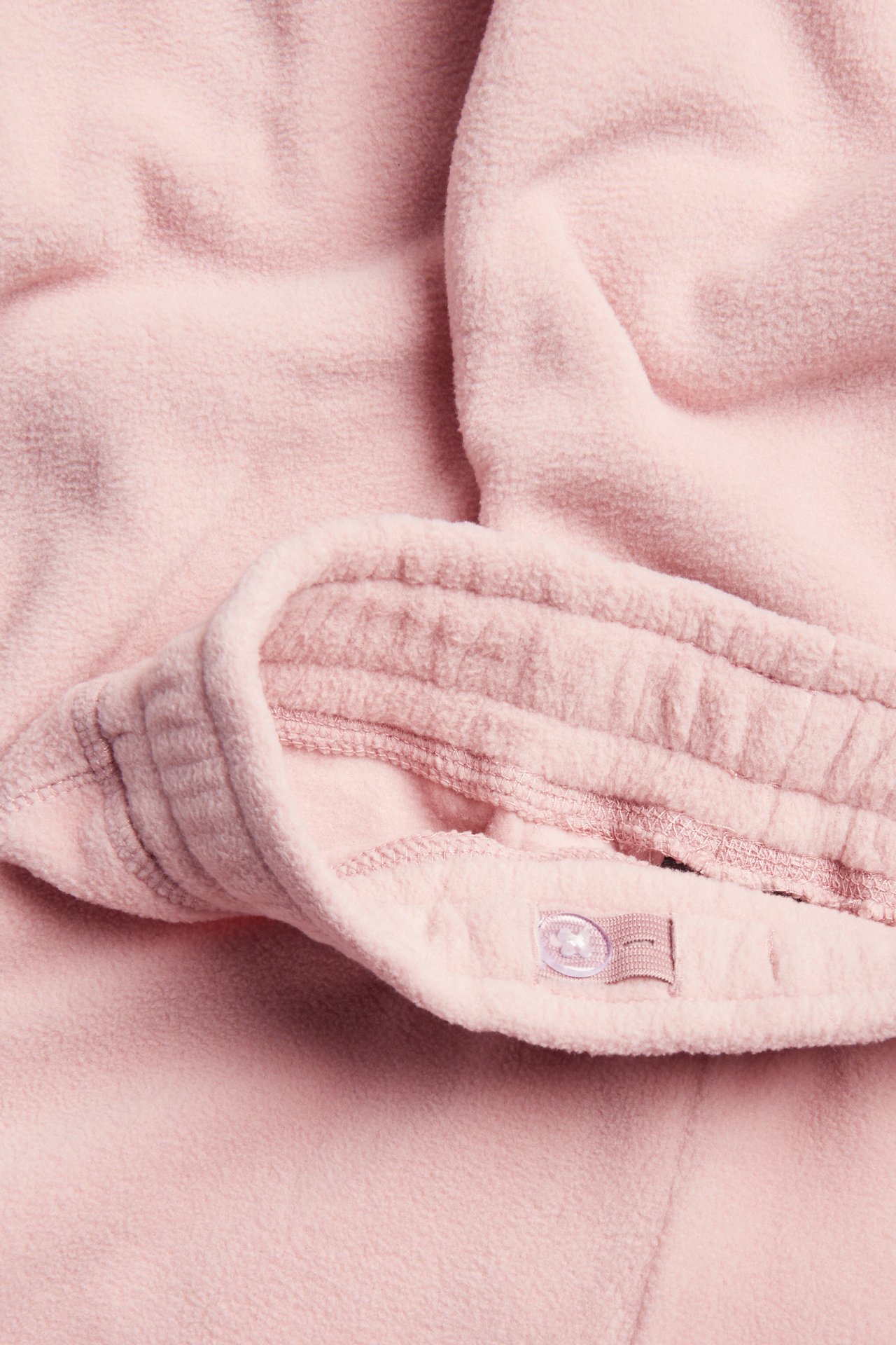 Närbild på rosa fleece-tyg med sömmar och en genomskinlig knapp på en ögla.