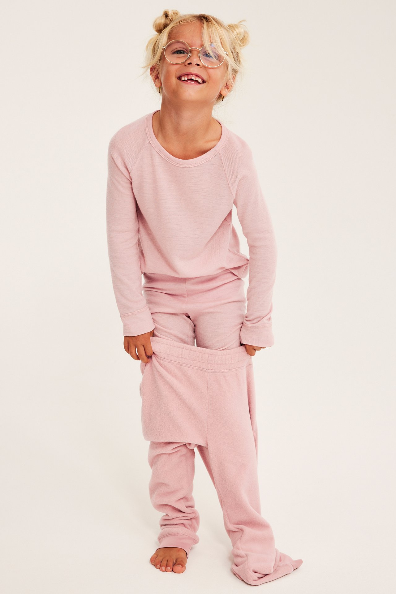 Frontvy på ett barn i rosa långärmad tröja och byxor, som drar ner rosa byxor.