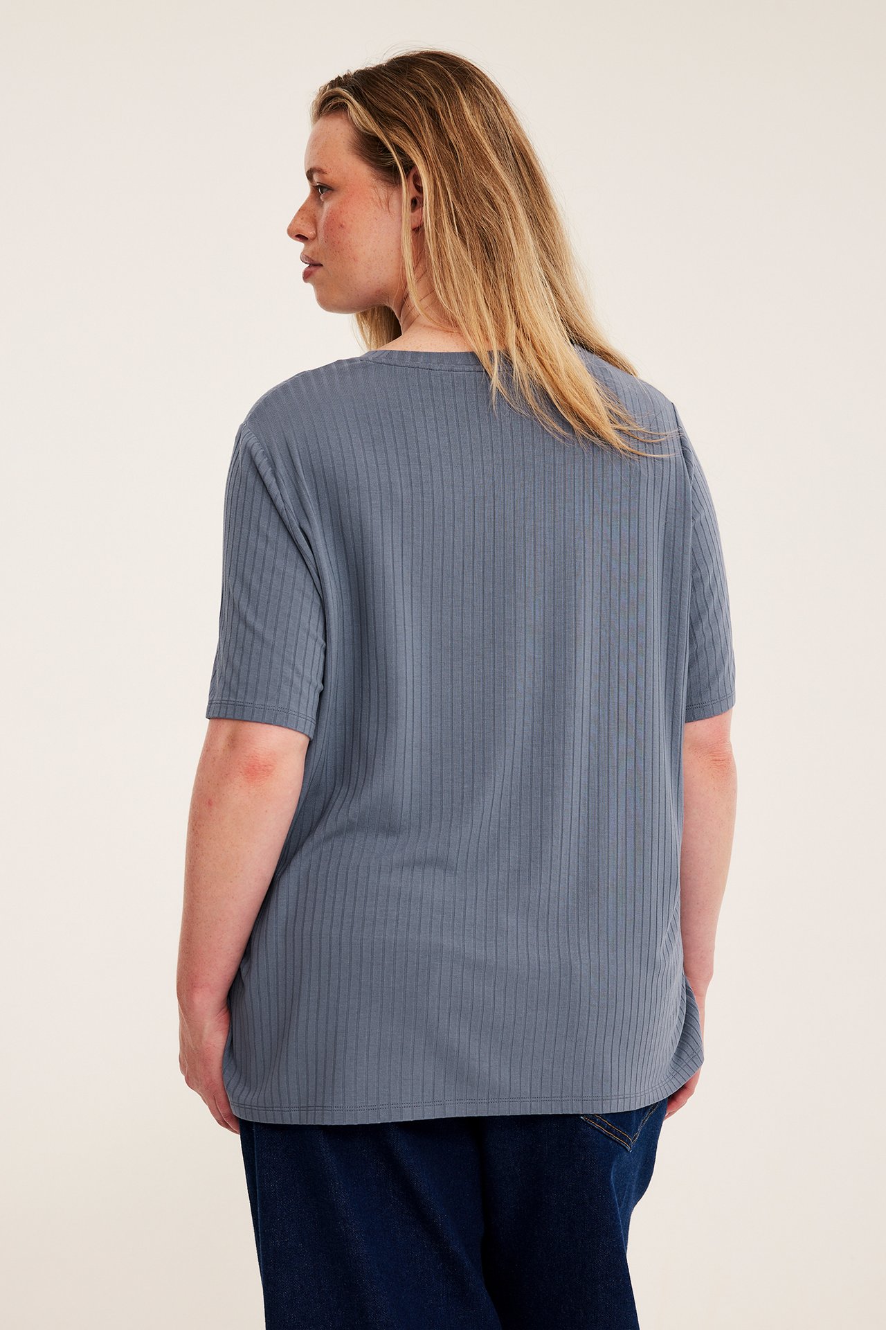 Kvinne sett bakfra i blå ribbet kortermet topp og mørkeblå jeans.