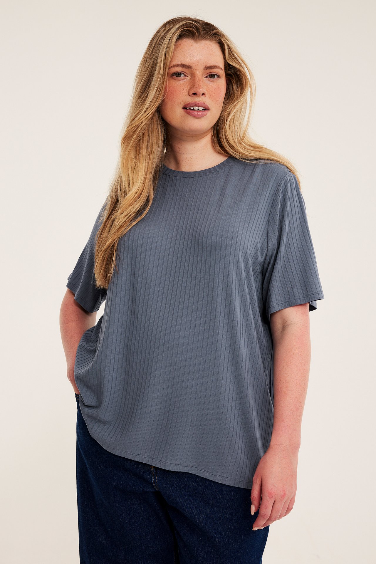 Frontbilde av kvinnelig modell med en blågrå ribbet oversized t-skjorte og mørkeblå jeans.