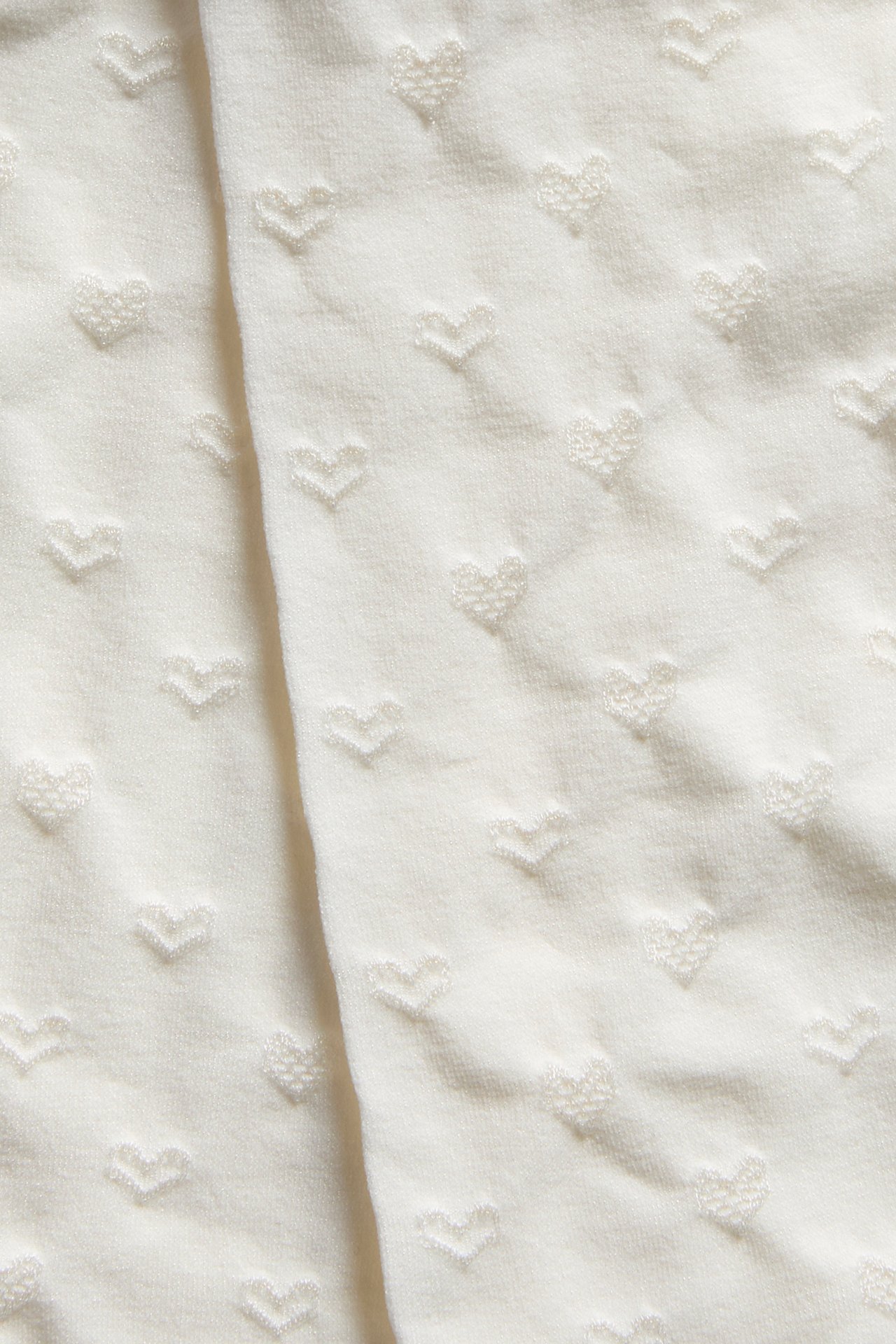 Lähikuva valkoisista sukkahousuista, joissa on kohokuvioitu sydänkuvio.