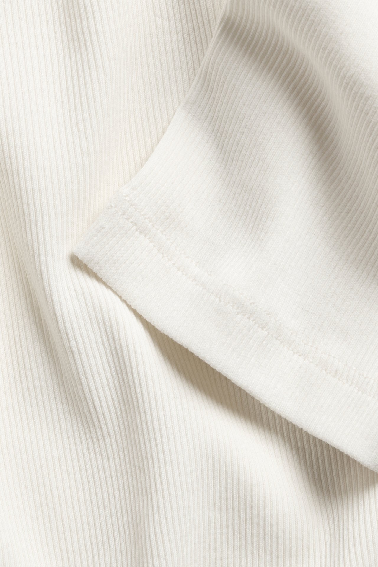 Nærbilde av en offwhite ribbet topp, som viser det strukturerte stoffet og en sydd ermekant.