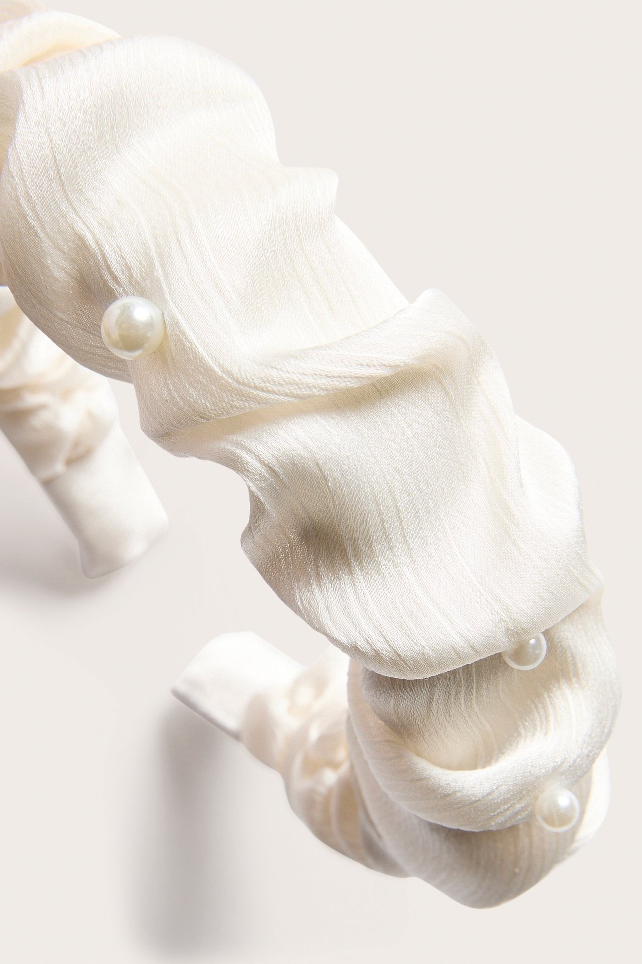 Lähikuva luonnonvalkoisesta rypytetystä satiinidiademista, jossa pieniä helmiä.