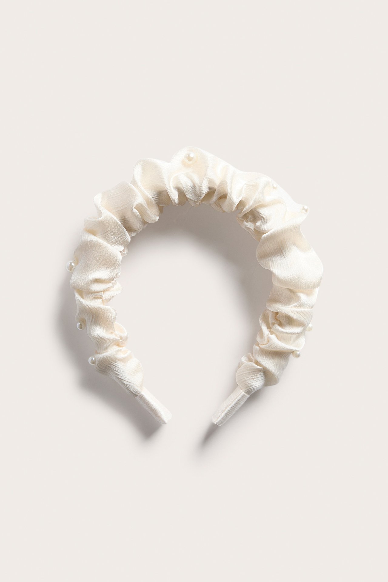 Frontvisning av et offwhite, rynket satengdiadem dekorert med små perler.