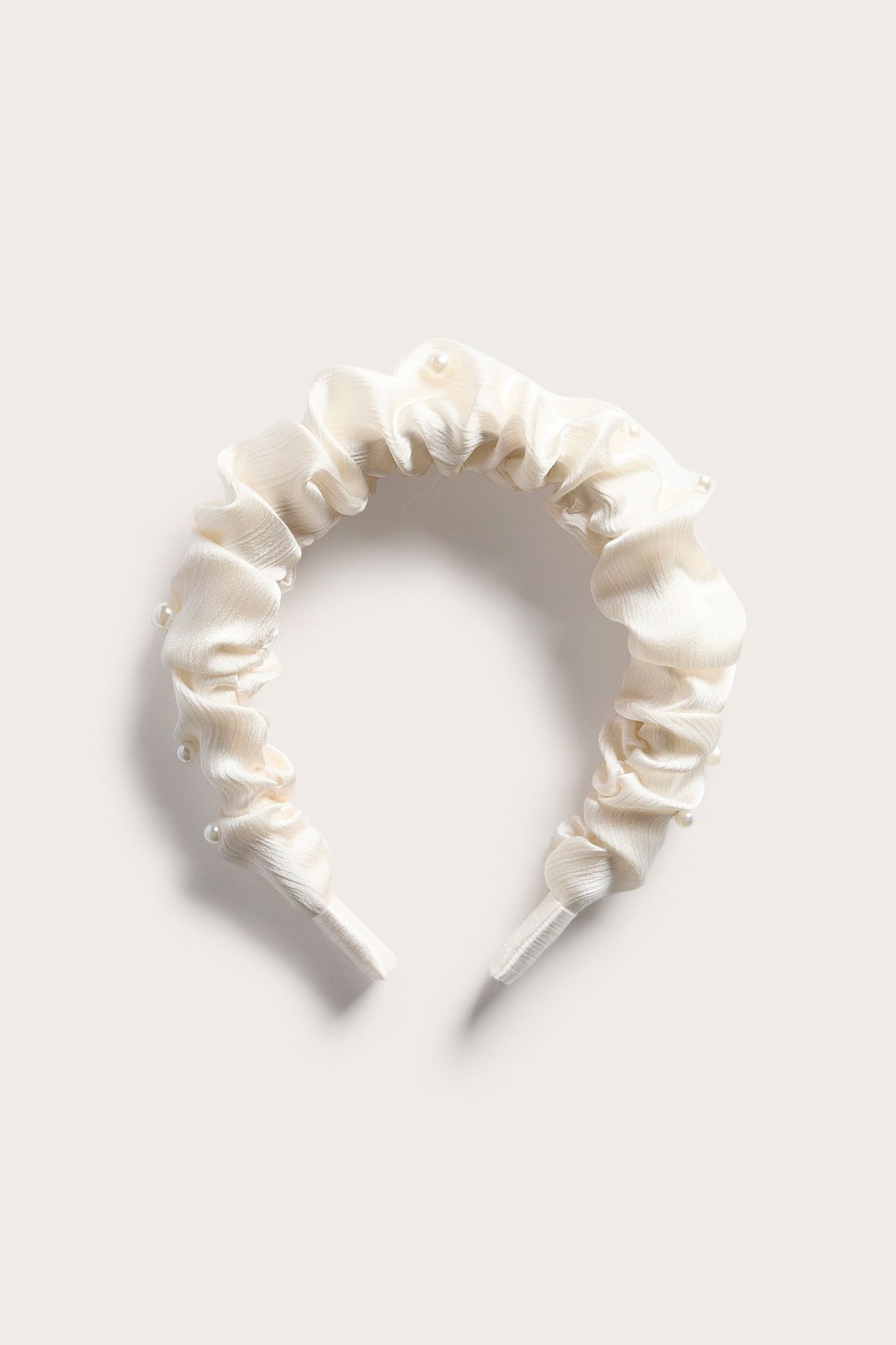 Edestä kuvattu offwhite, rypytetty satiinipanta, koristeltu pienillä helmikoristeilla.