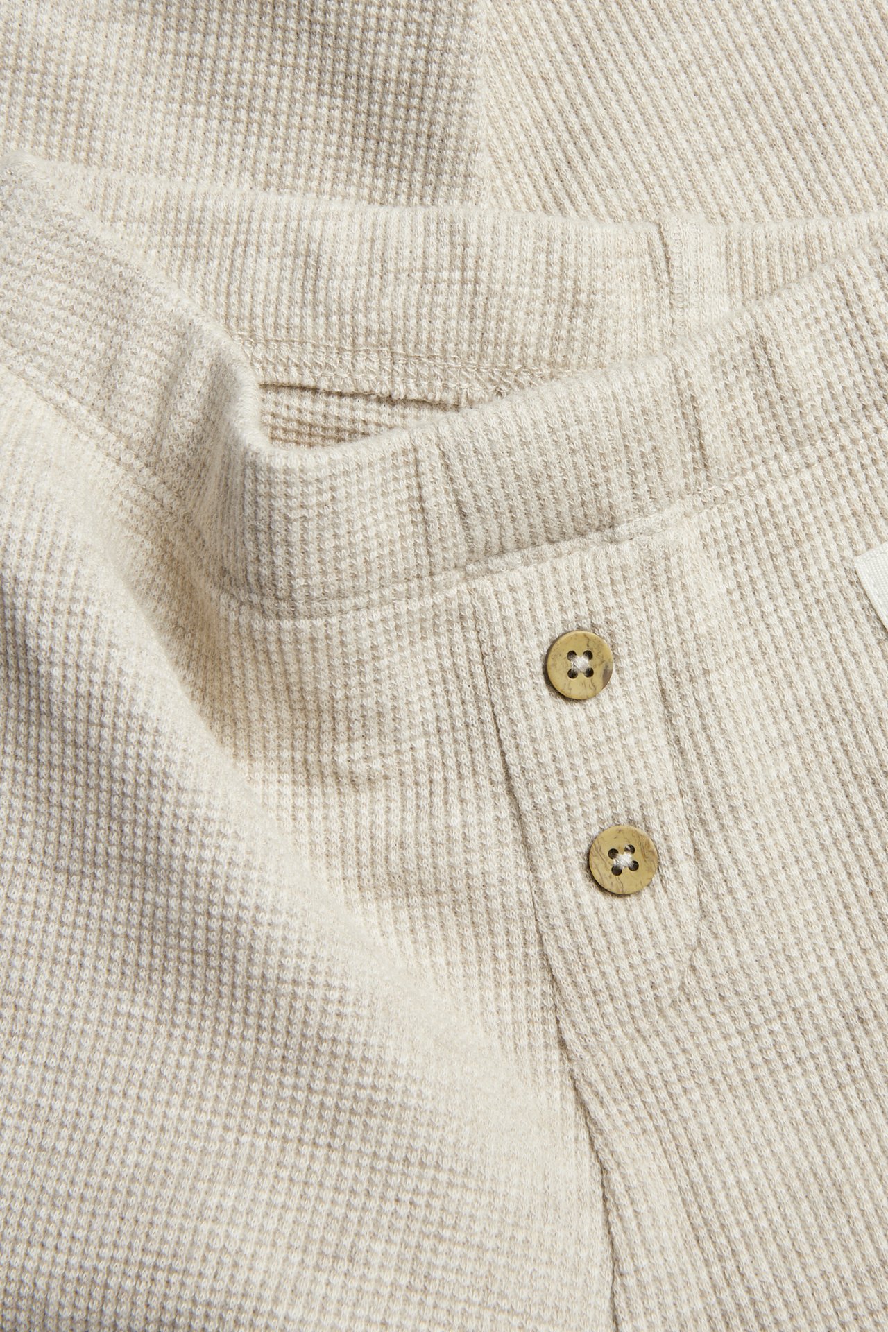 Nærbilde av beige vaffelstrikkede baby-leggings med to dekorative knapper foran.