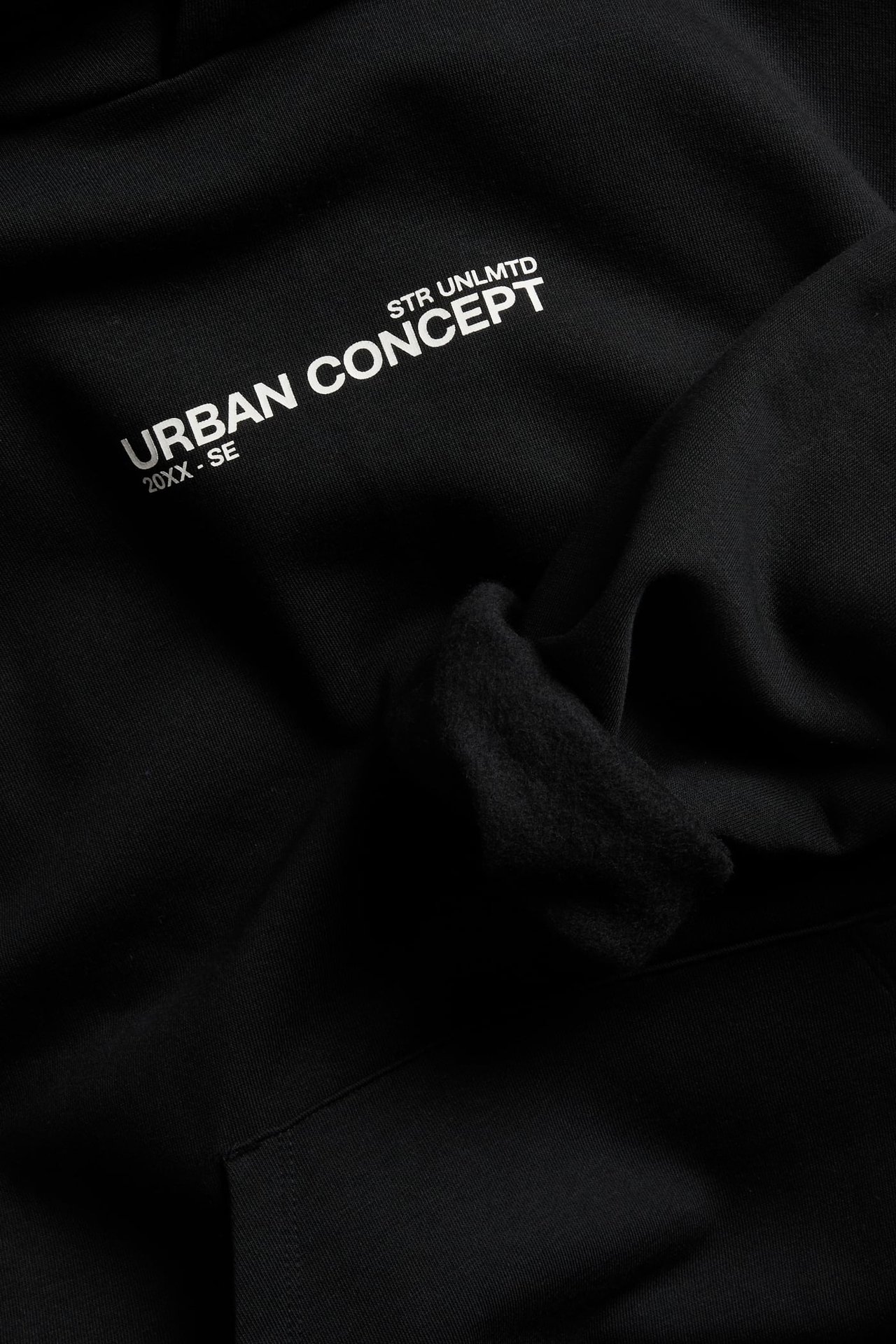 Zbliżenie na czarną bluzę z kapturem z białym nadrukiem „STR UNLMTD” i „URBAN CONCEPT”.