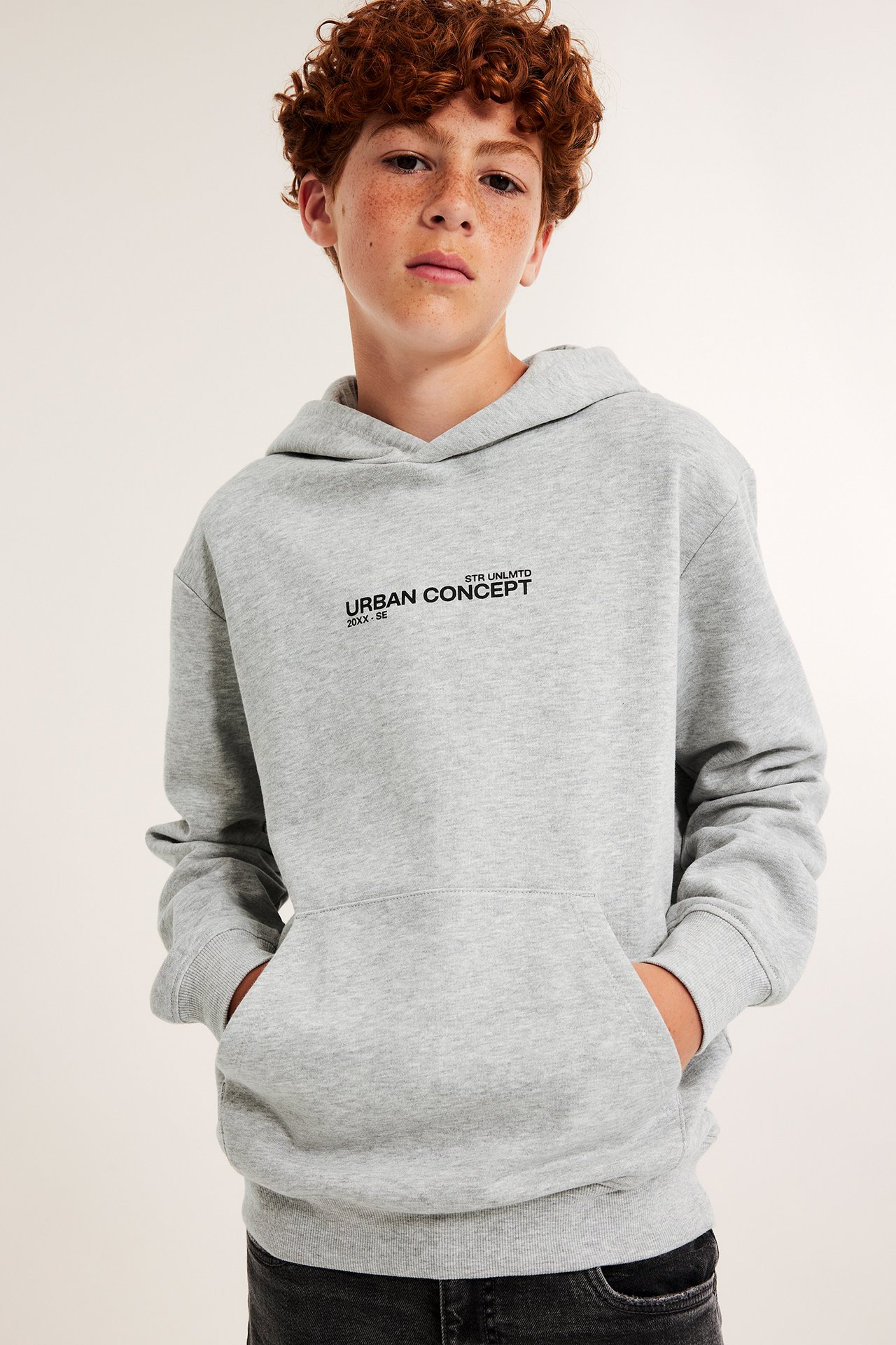 Framifrån, barn i grå hoodie med tryck och svarta jeans.