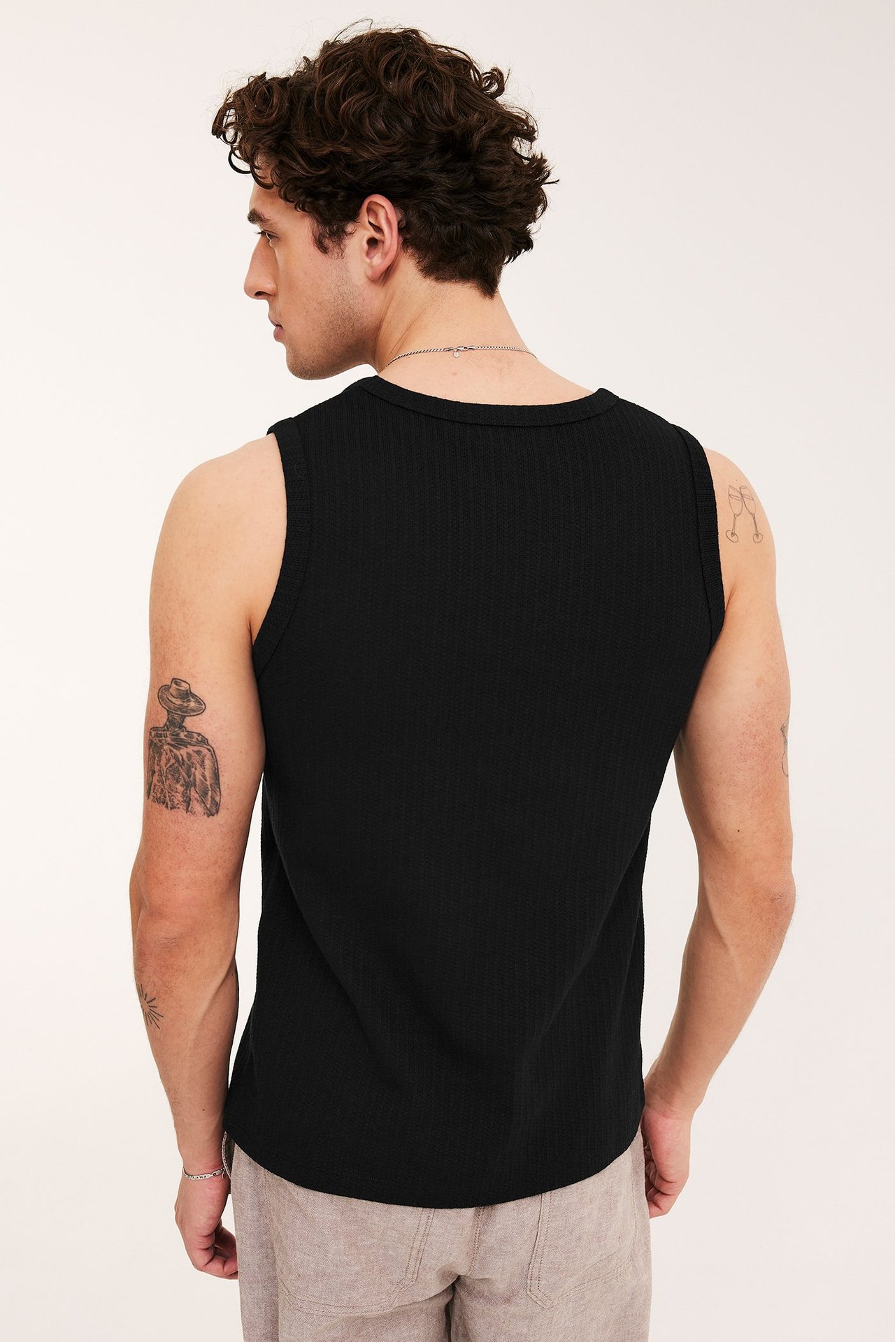 Ryggvy av en man i svart slim fit pointelle-linne och ljusbeige byxor.