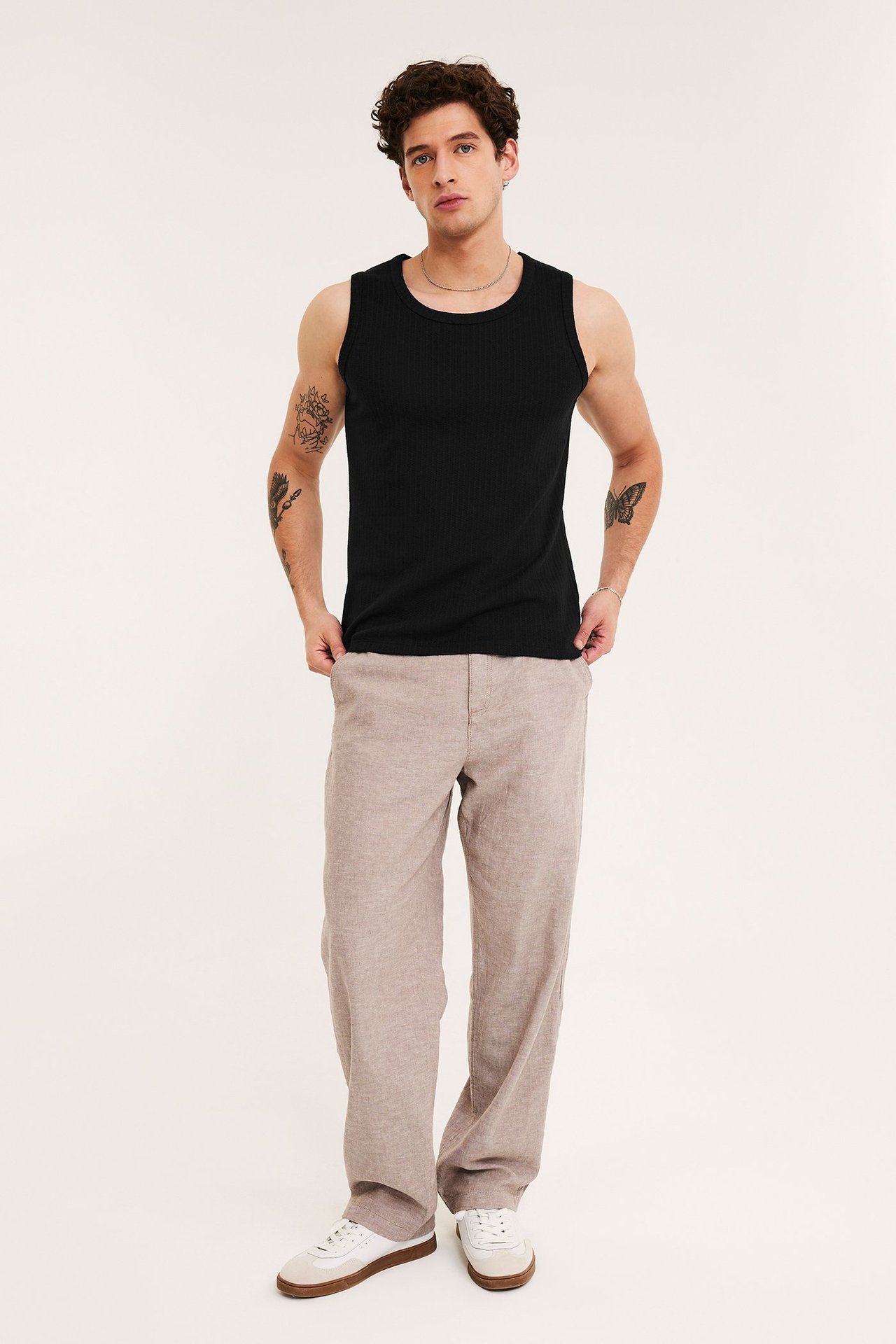 Frontutsikt av en mann i svart pointelle-singlet, beige bukser og hvite joggesko.