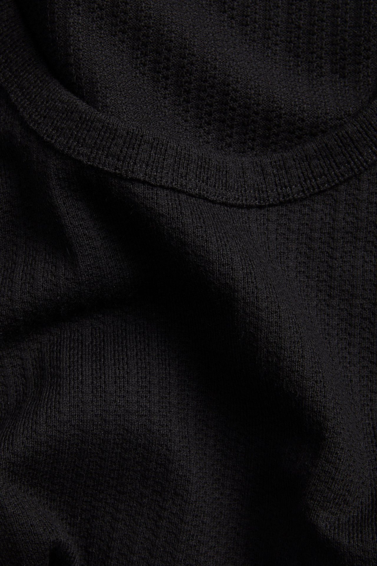 Närbild av ett svart pointelle jacquard-linne, som visar det texturerade tyget och ribbade halsringningen.