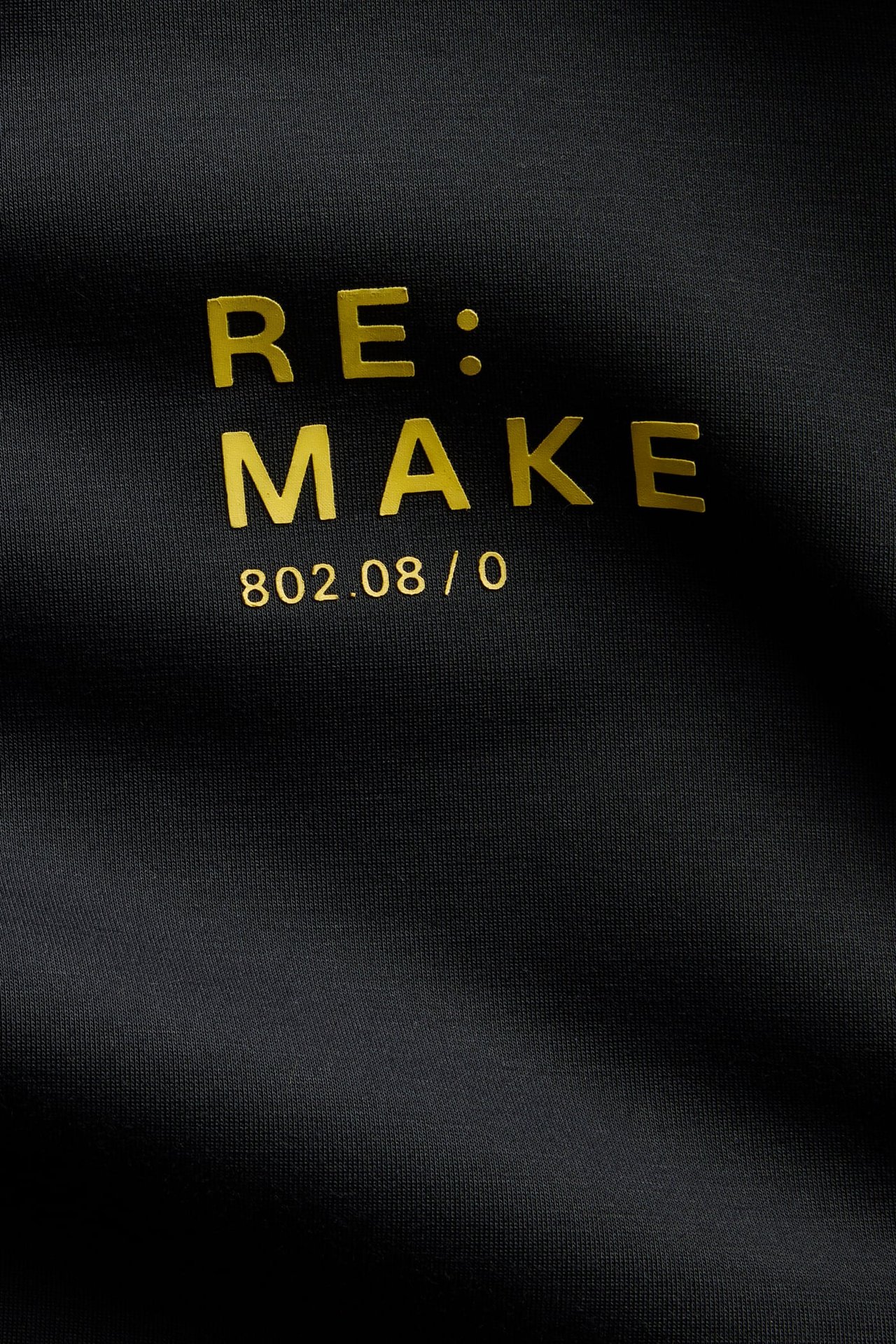 Zbliżenie czarnego ubrania ze złotym napisem 'RE: MAKE' i numerami '802.08 / 0'.