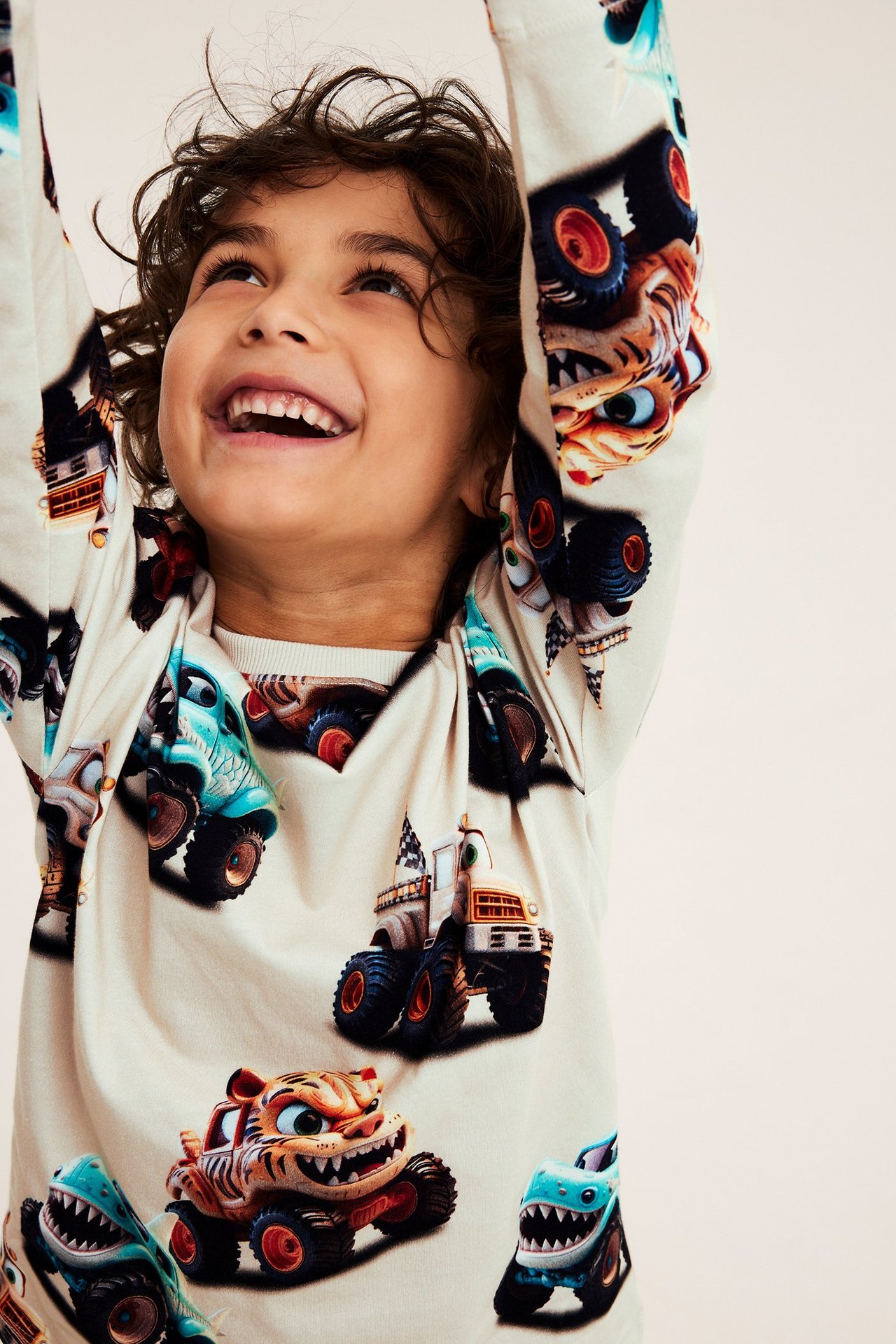 Leende barn i lös ljusbeige långärmad bomulls-t-shirt med monstertryck. Framifrån.
