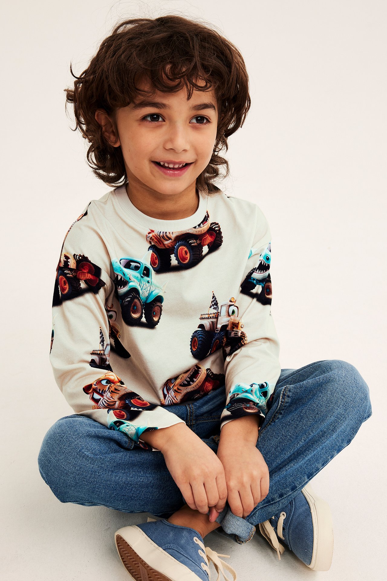 Dziecko w beżowej koszulce z długim rękawem w potwory, niebieskich dżinsach i niebieskich tenisówkach.