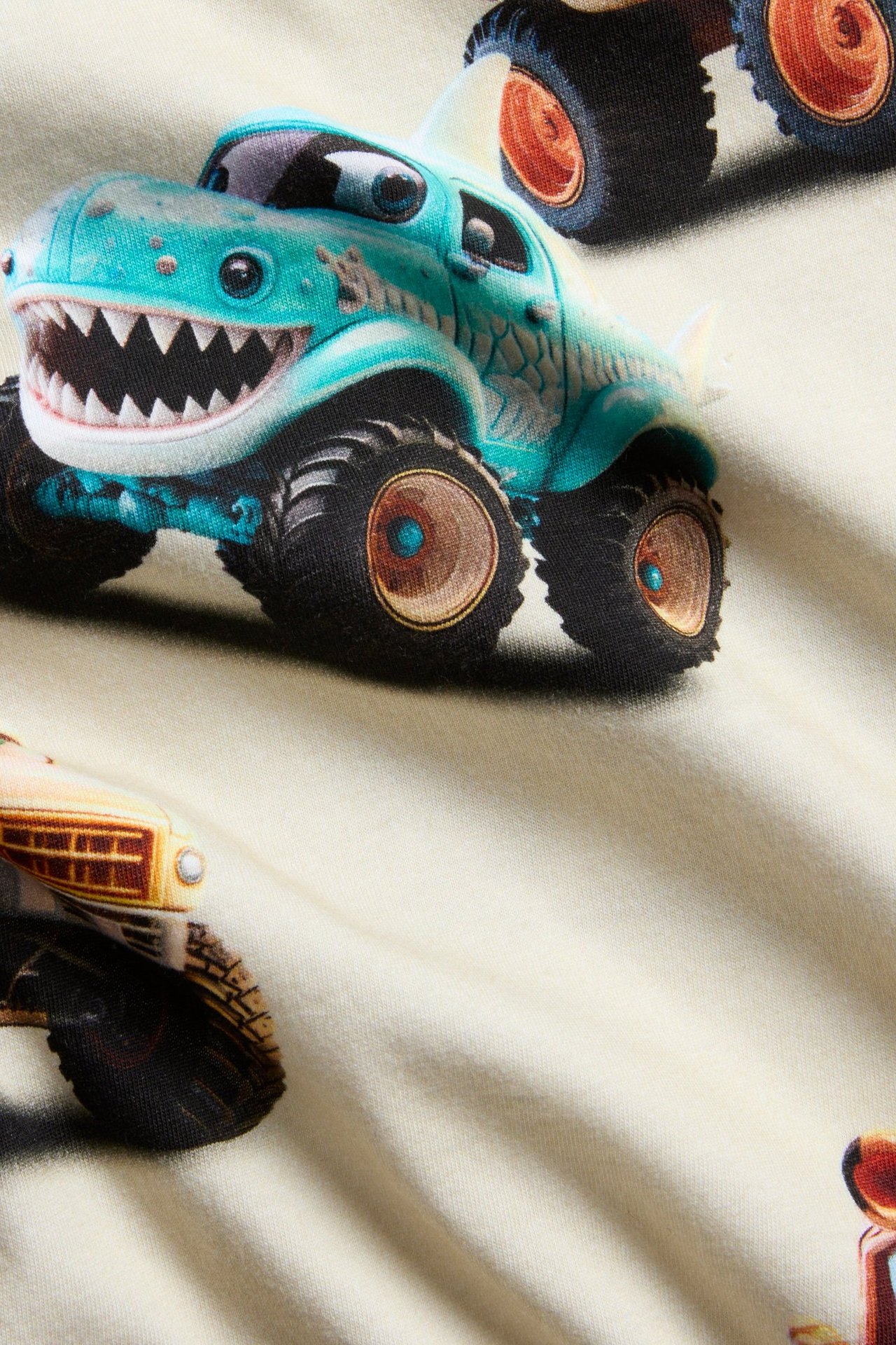 Närbild på en ljusbeige långärmad barntröja i bomull med färgglatt monstertruck-tryck.