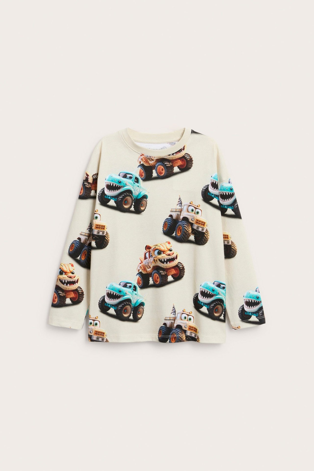 Framifrån: Ljusbeige långärmad barntröja i bomullstrikå med ett allover-tryck av monstertruckar.