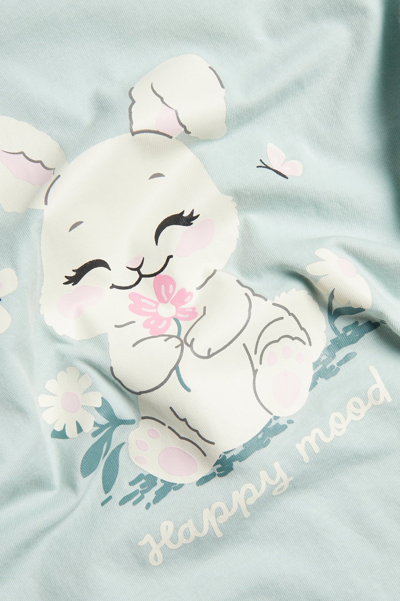 Zbliżenie na jasnozieloną dziecięcą koszulkę z bawełny z białym nadrukiem królika i napisem 'happy mood'.
