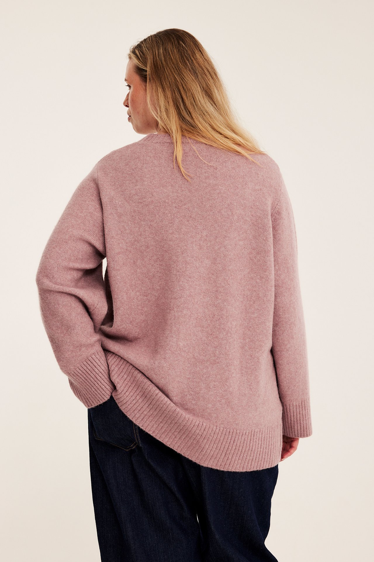 Baksidan av kvinna i en oversized rosa långärmad tröja och mörkblå jeans.