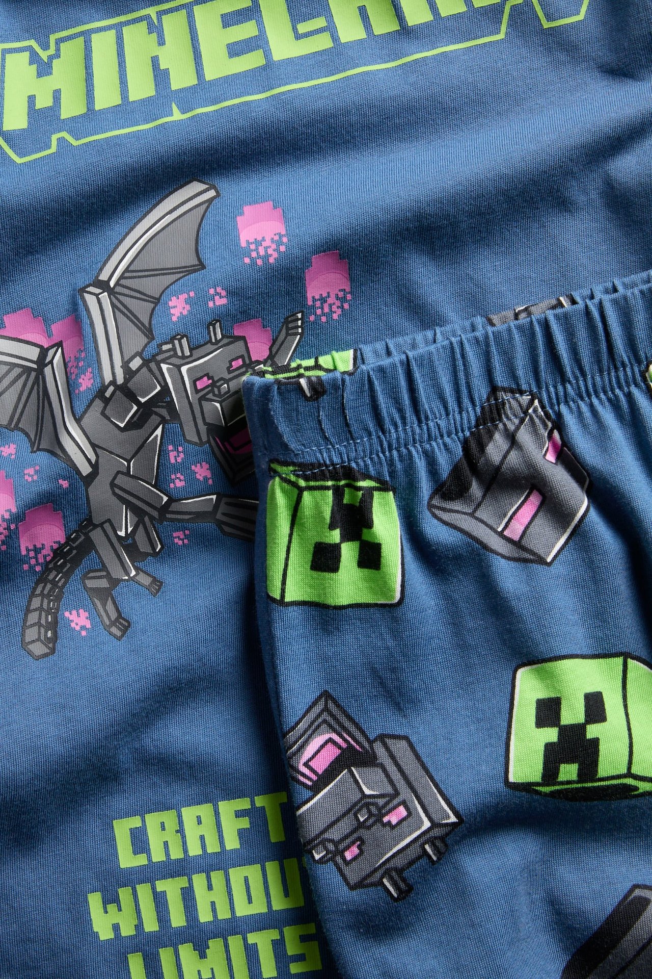 Nærbilde av mørkeblå pyjamas i bomull med Minecraft dragemotiv og bukser med blokkmønster.