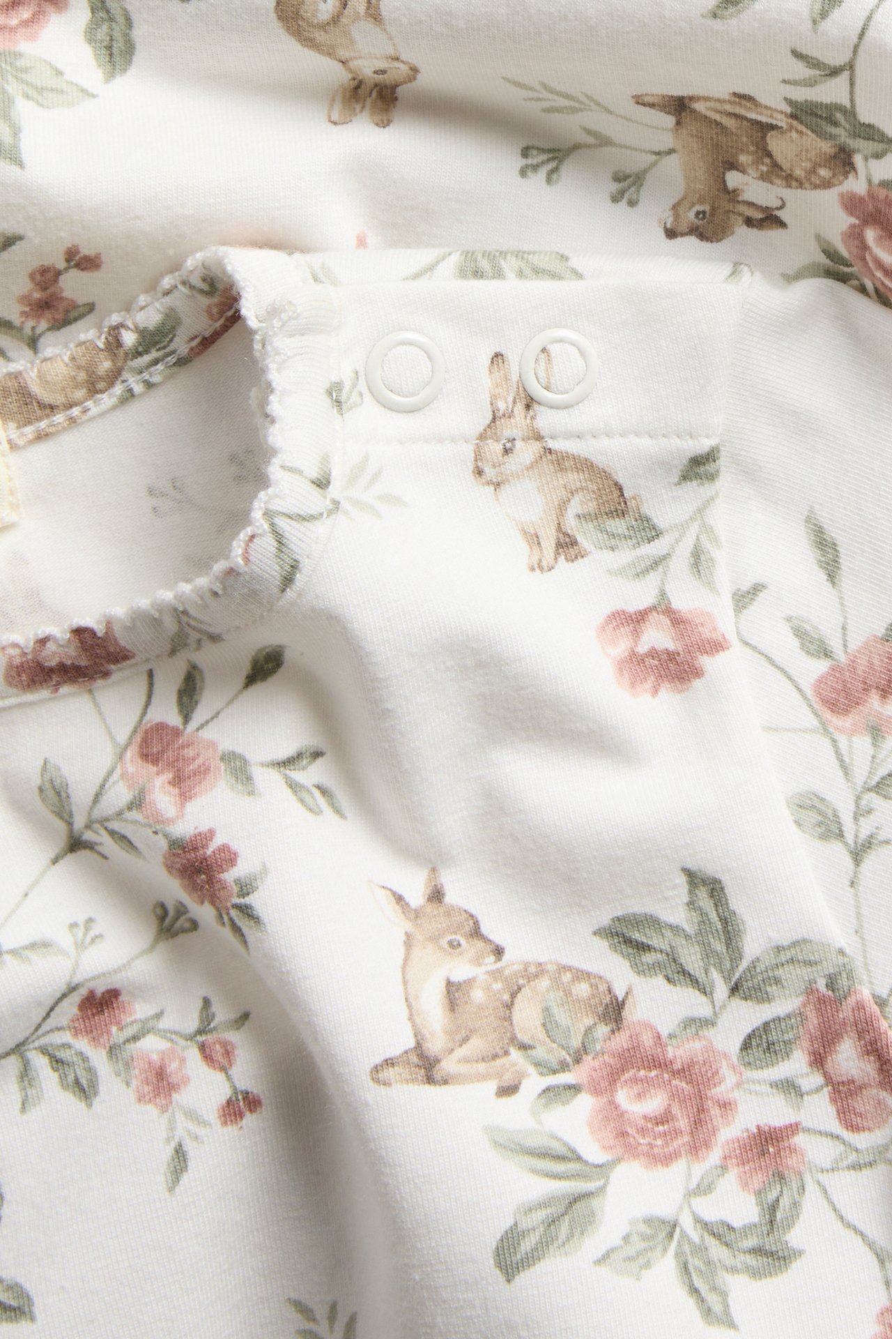 Nærbilde av en offwhite baby langermet body med rådyr- og blomsterprint, picotkant og trykknapper.