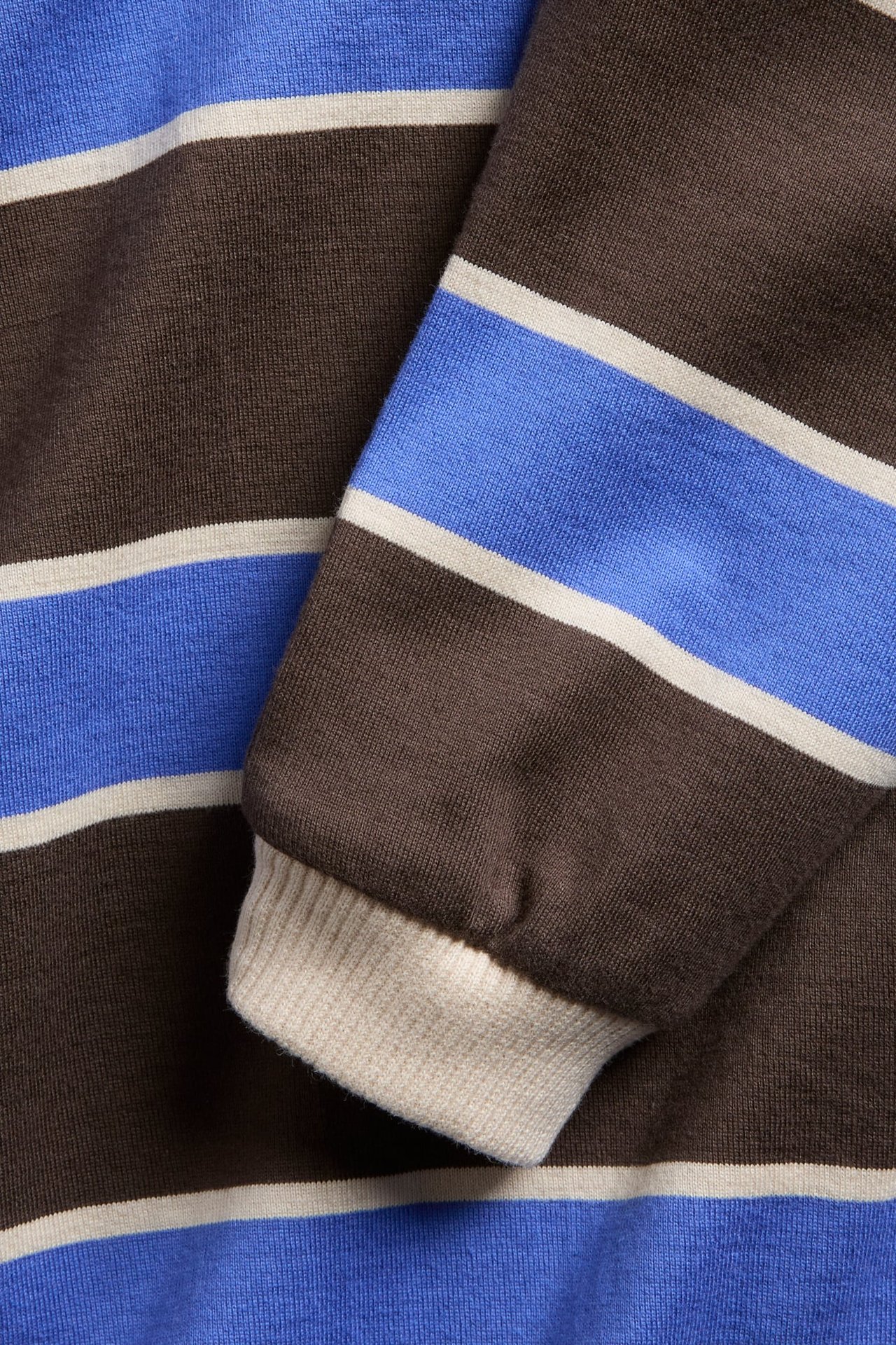 Nærbilde av en brun, blå og beige stripete langermet strikket genser med ribbestrikkede mansjetter.