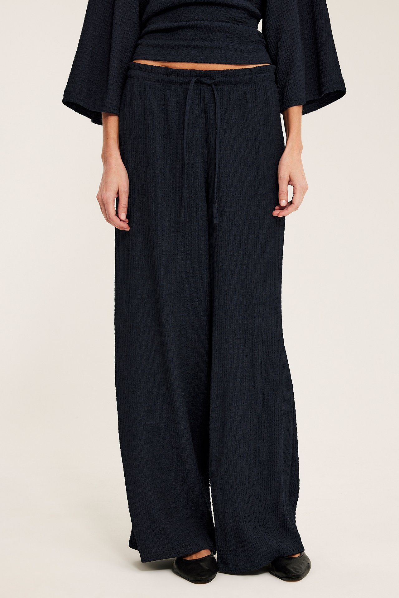 Edestä: nainen yllään tummansiniset joustavat trikoohousut, yhteensopiva toppi ja mustat ballerinat.