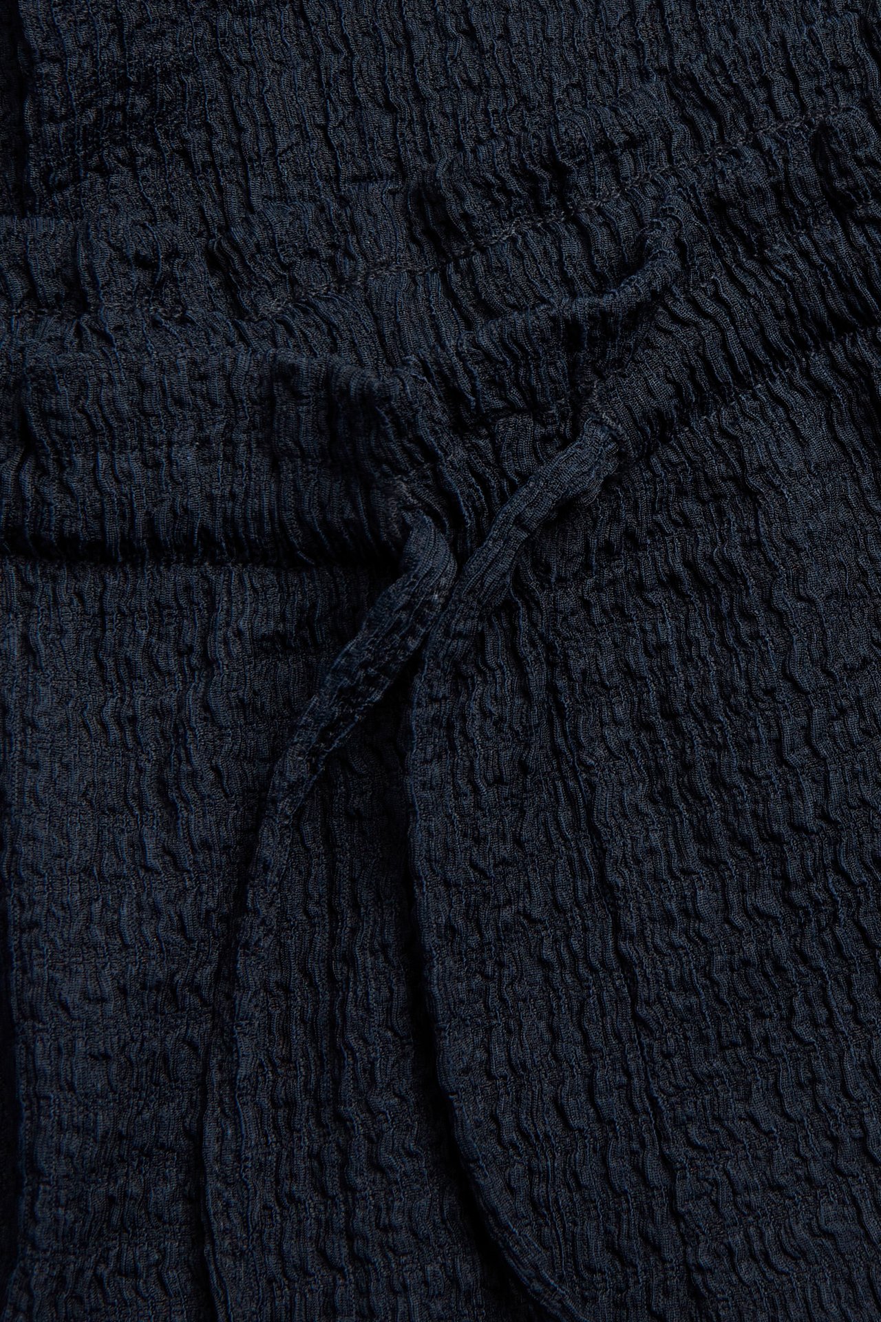 Lähikuva tummansinisistä strukturoiduista jerseyhousuista, joissa kiristysnyöri ja röyhelöreuna vyötäröllä.