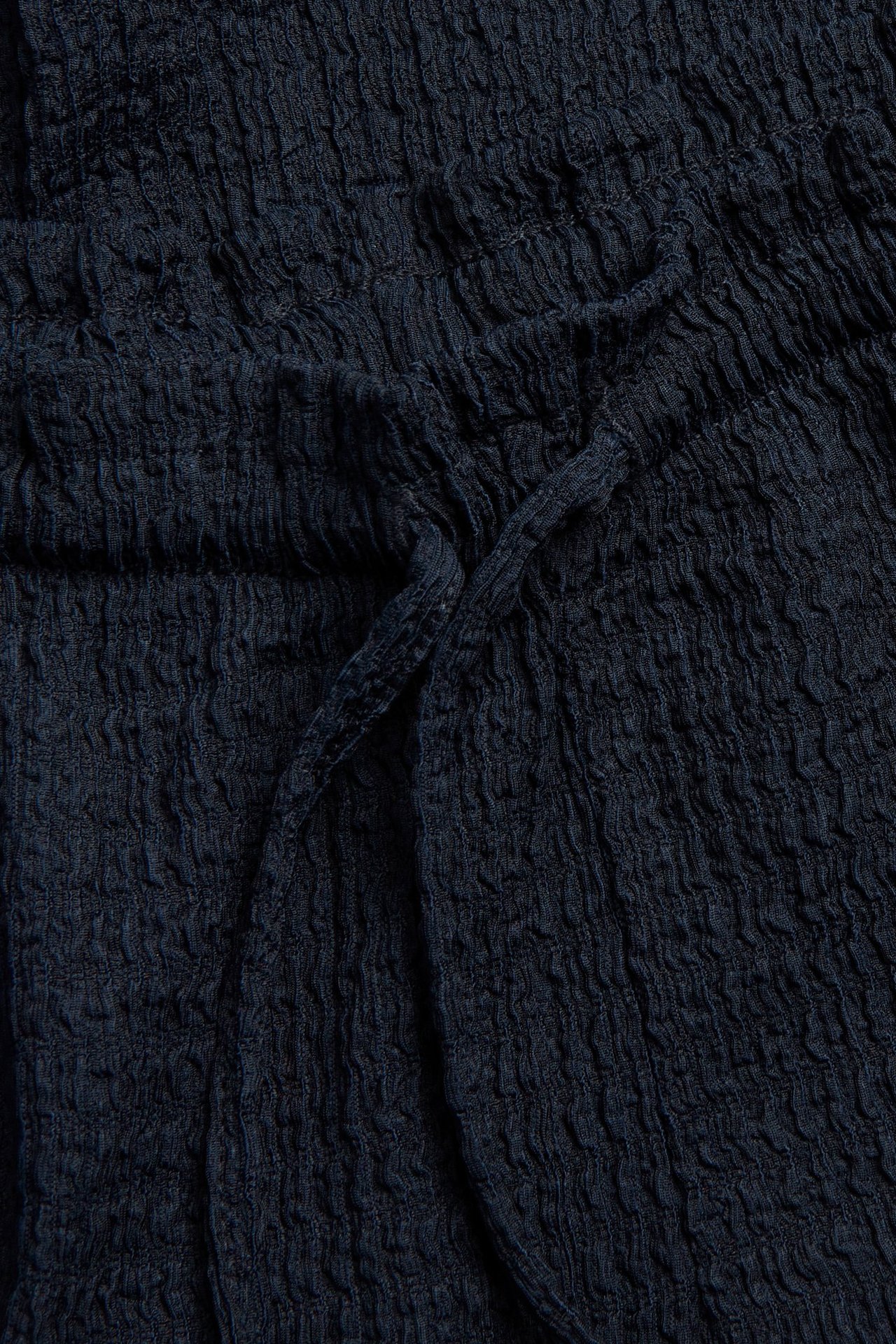 Närbild av mörkblå strukturerade jerseybyxor med knuten dragsko och volangkant i midjan.