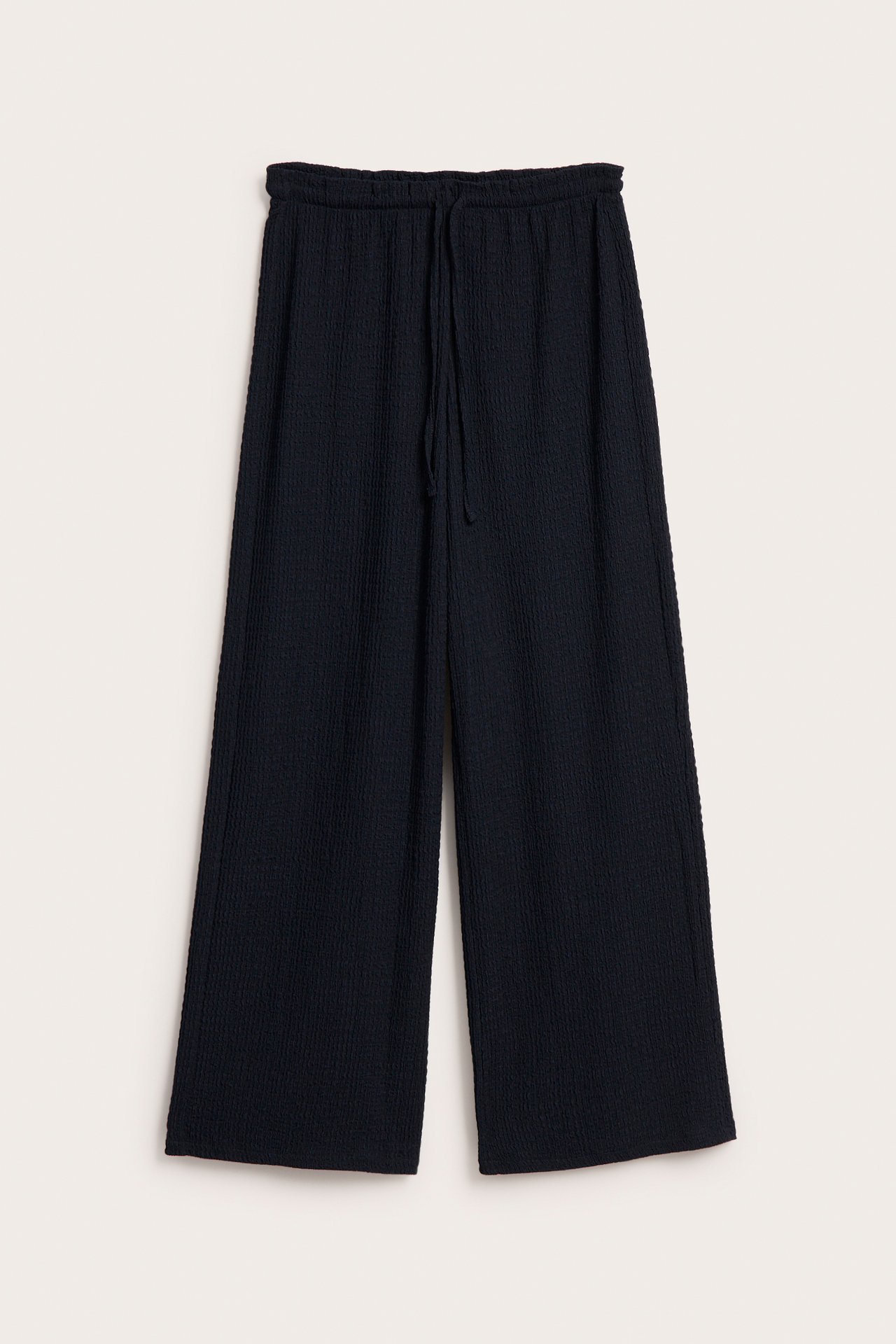 Edestä kuvatut tummansiniset, leveälahkeiset vetohousut strukturisoitua jerseytä, jossa kiristysnyöri vyötäröllä.