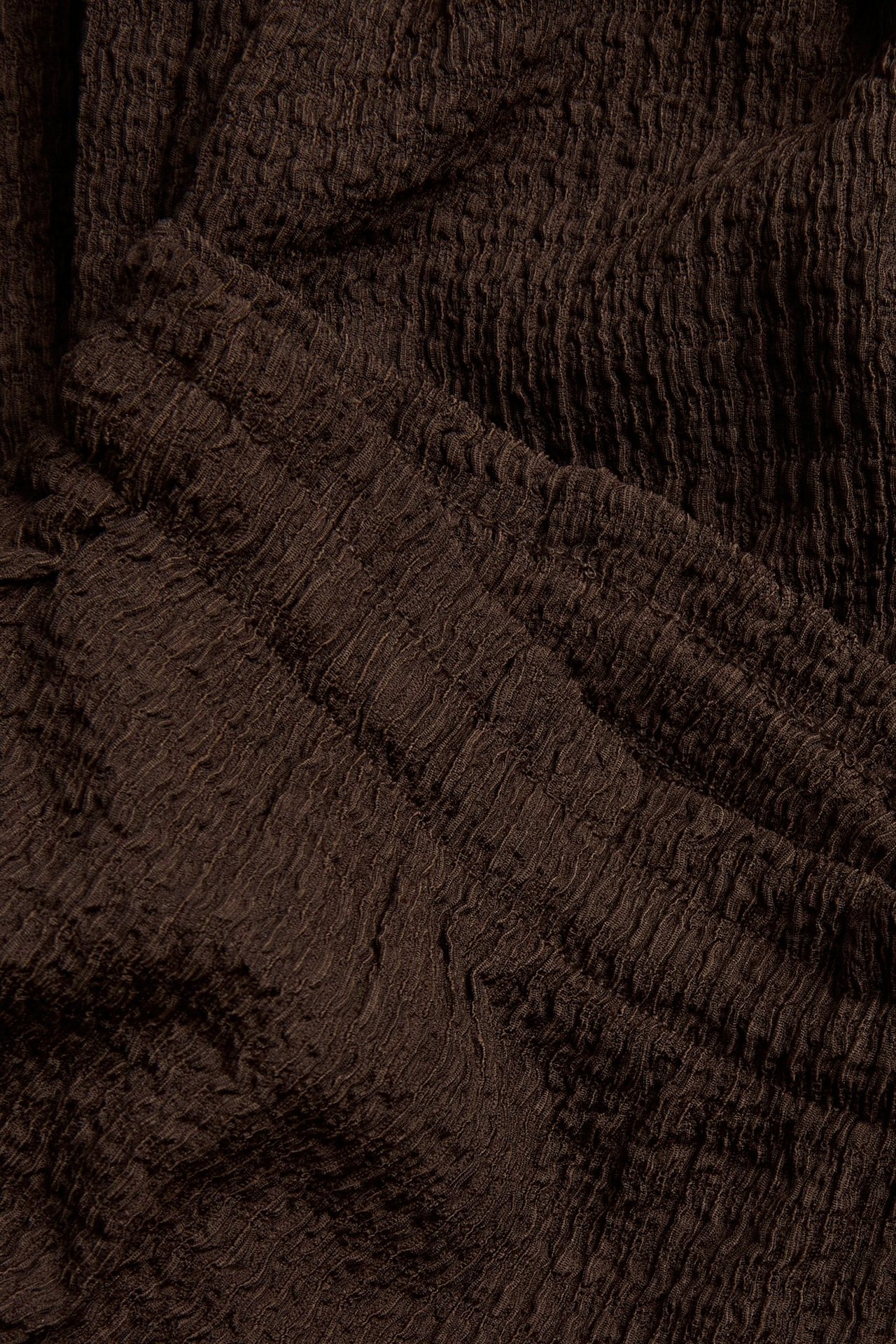Närbild av mörkbrunt strukturerat jerseymaterial som visar dess texturerade, veckade yta.